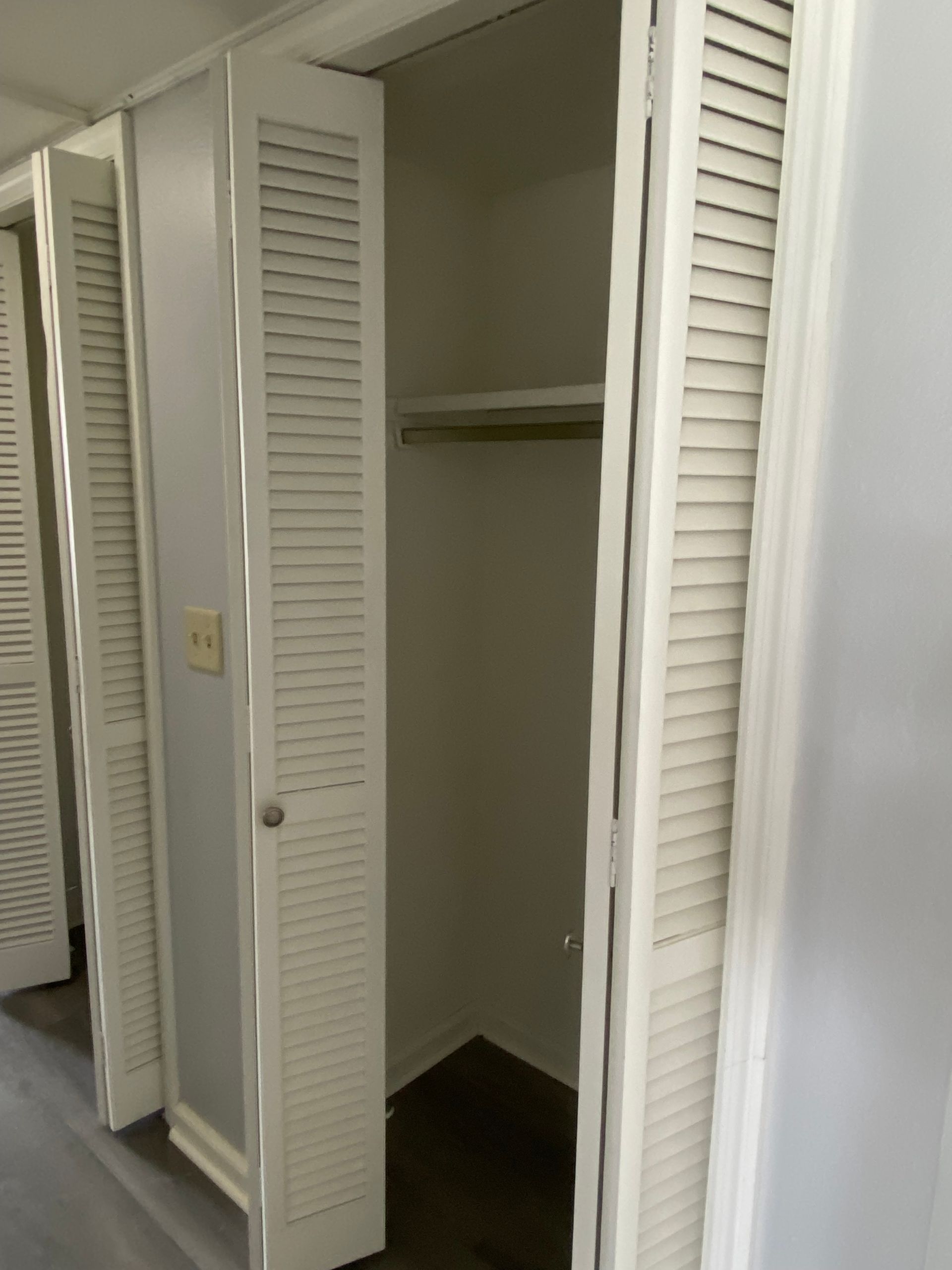 Open closet with white louvered doors and empty shelves in a small room.