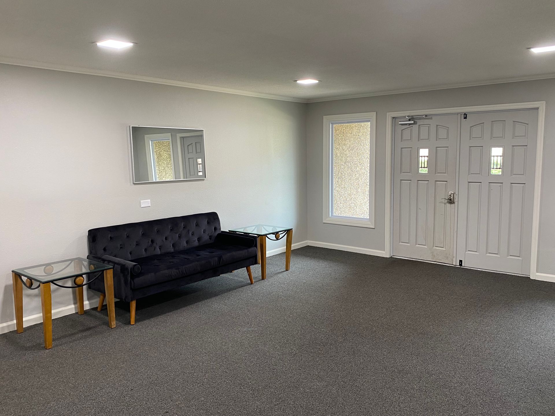 Empty room with a black sofa, small tables, gray carpet, and double glass doors.