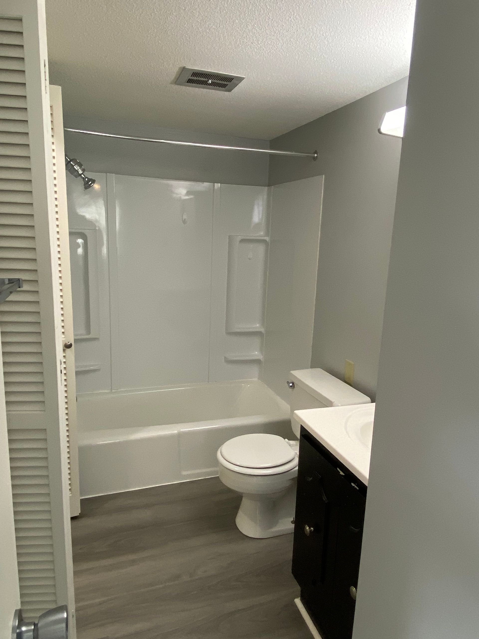 Small bathroom with bathtub, toilet, sink vanity, and gray walls and floor.