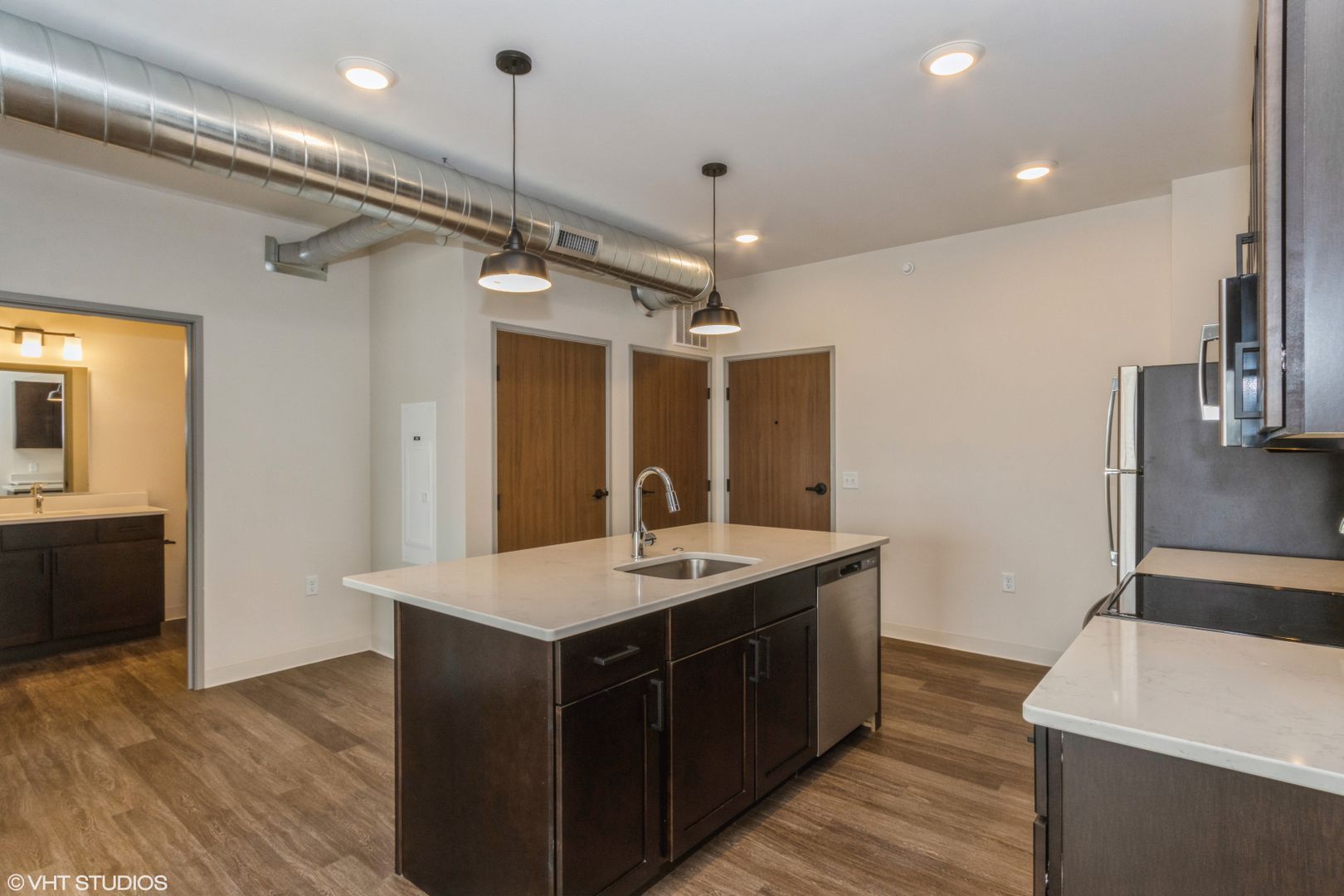Narrow galley kitchen with white cabinets, gray floor, stove, sink, refrigerator, and overhead light.