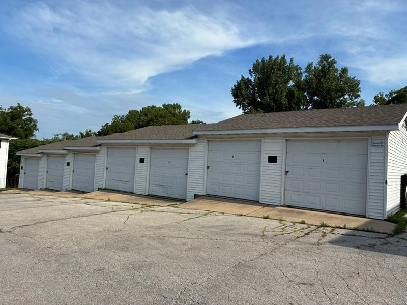 White garage units with closed doors along a cracked paved lot under a partly cloudy sky