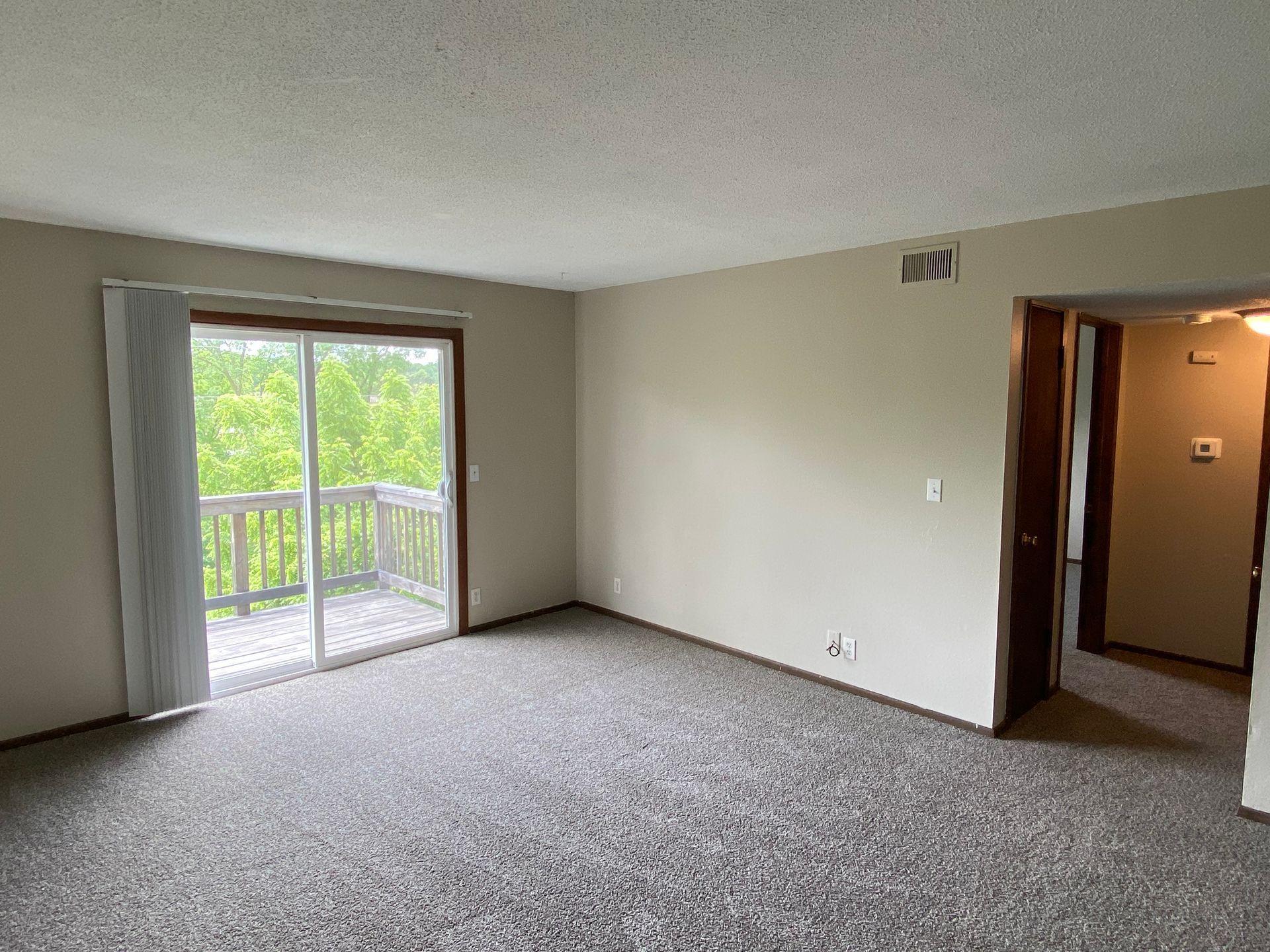 Empty carpeted living room with sliding glass doors to a balcony and an open doorway to a hall