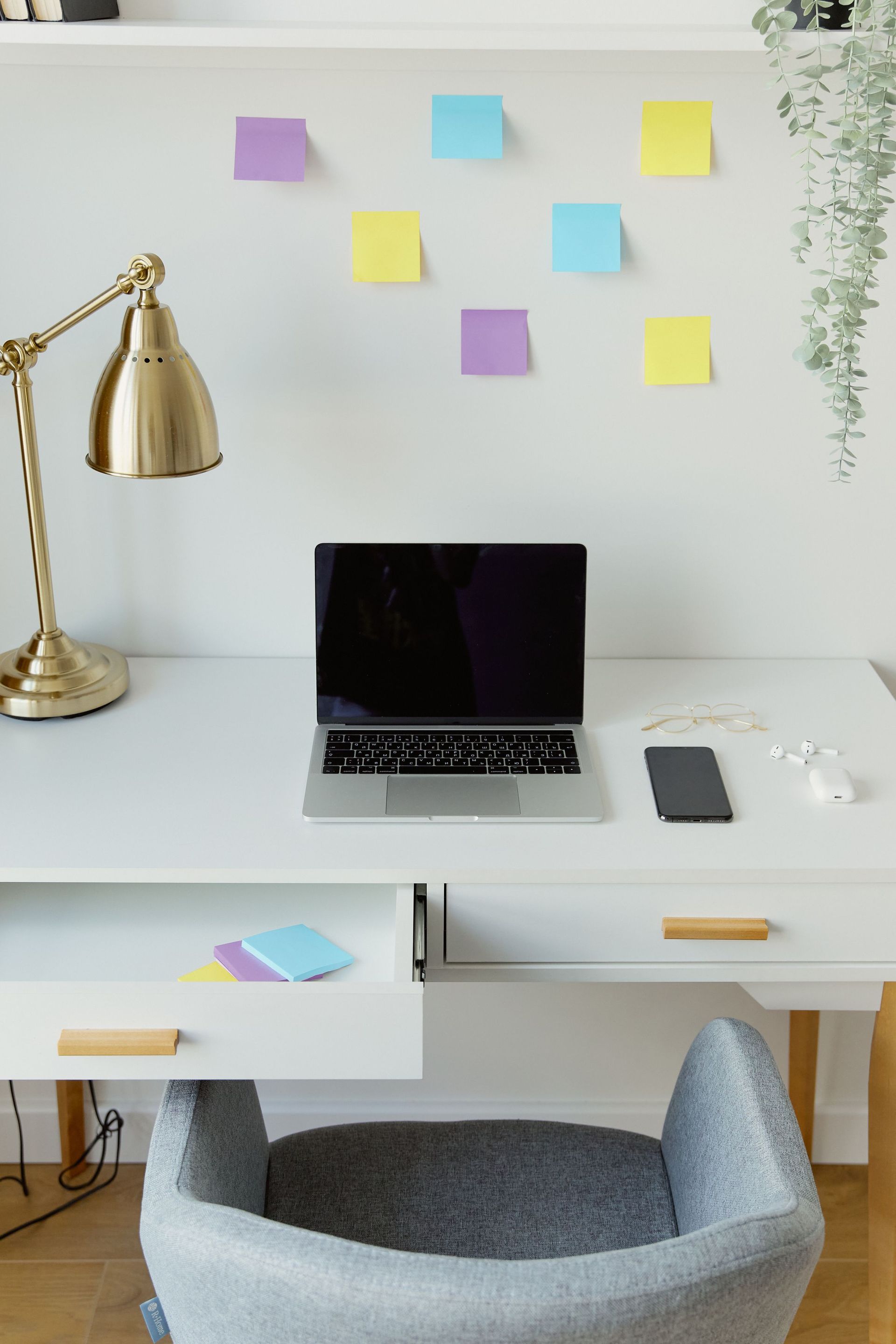 Minimal home office desk with laptop, gold lamp, sticky notes, phone, and chair