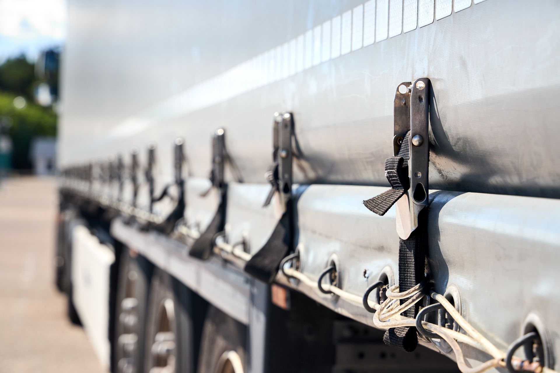 Industrial tarp systems with ratchet straps and tie-downs securing a gray tarp on a semi trailer
