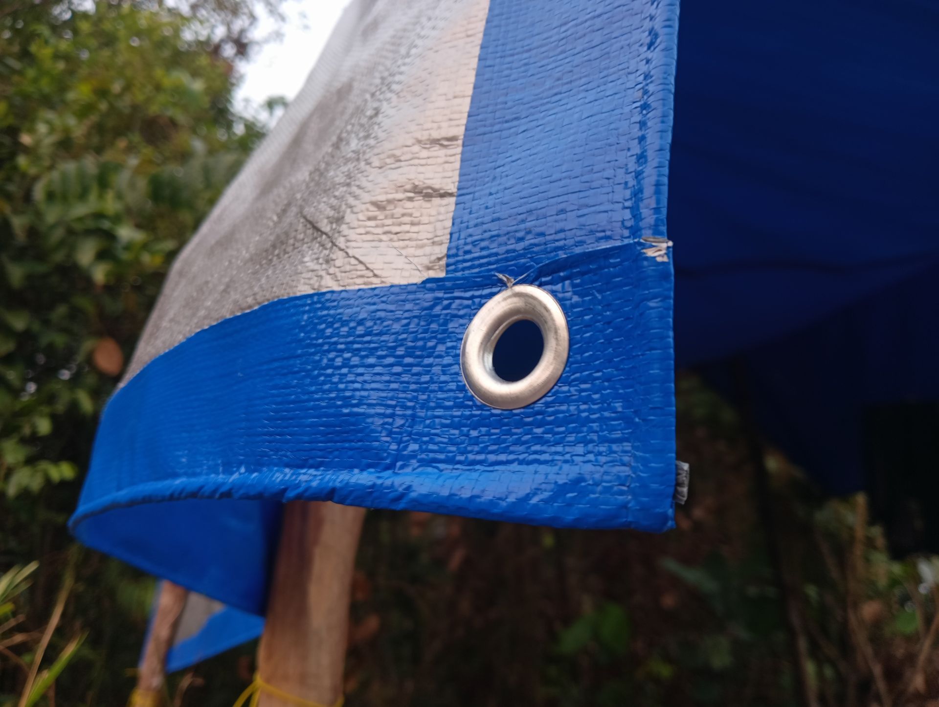 Close-up of a blue reinforced hem and metal grommet on industrial tarp systems