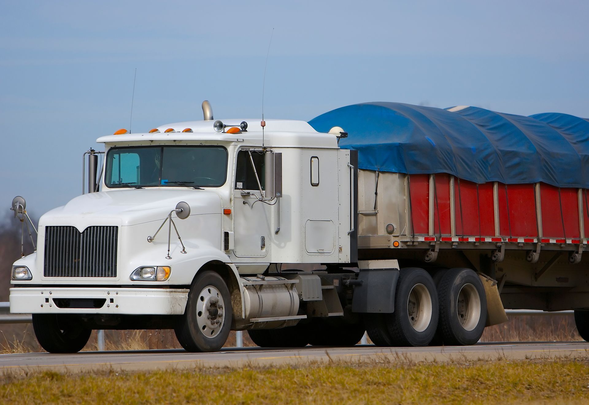 A tractor trailer with a canvas covering a load on its truck bed.