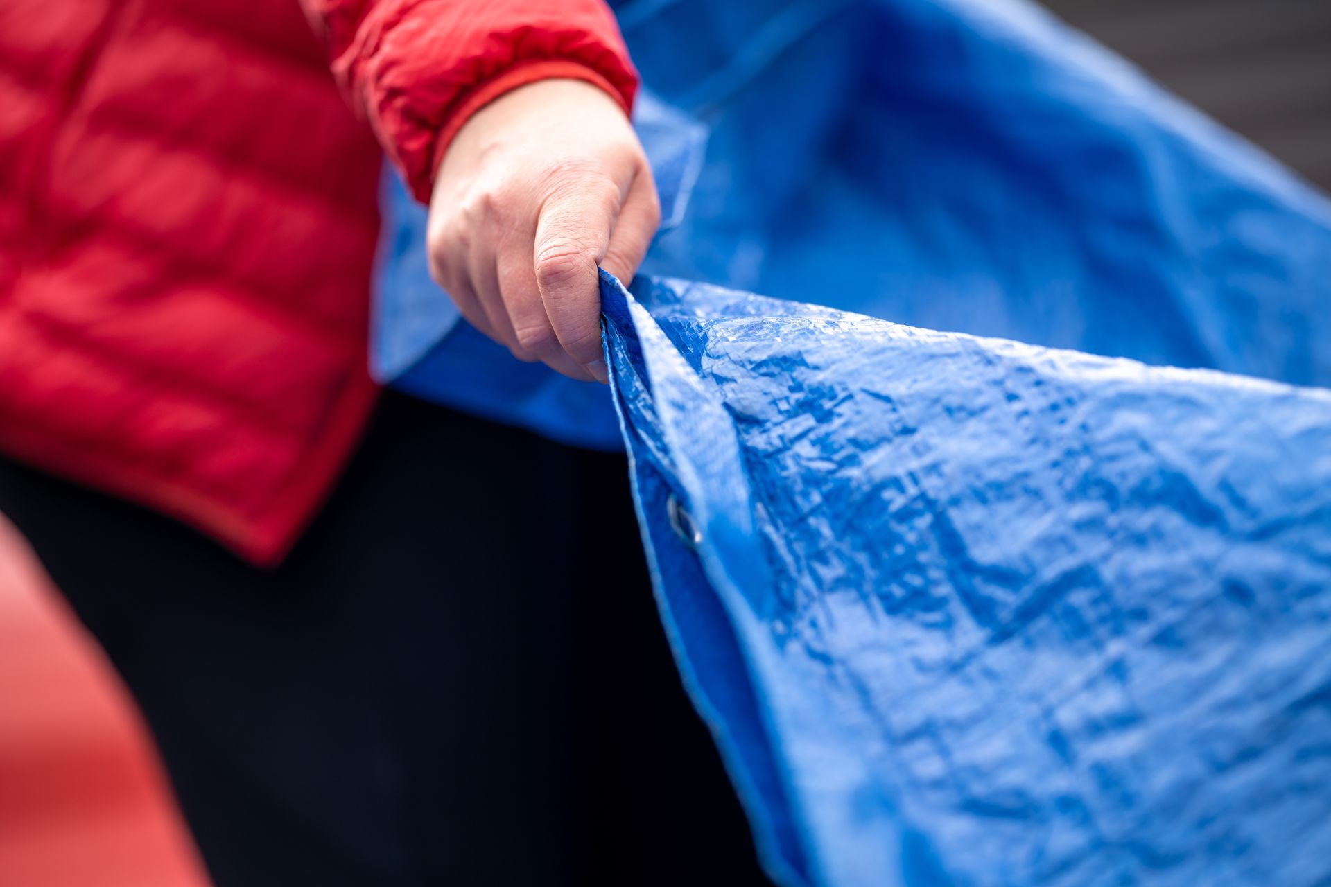 Hand holding the grommeted edge of a blue tarp used in custom industrial tarp systems