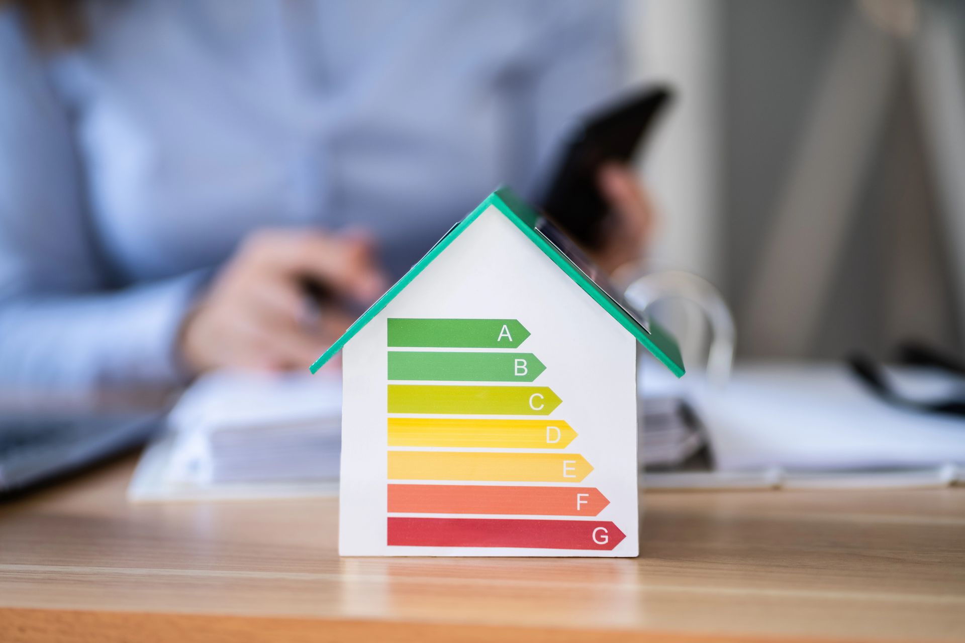 Colorful energy efficiency house model on a desk, with a blurred person working in the background