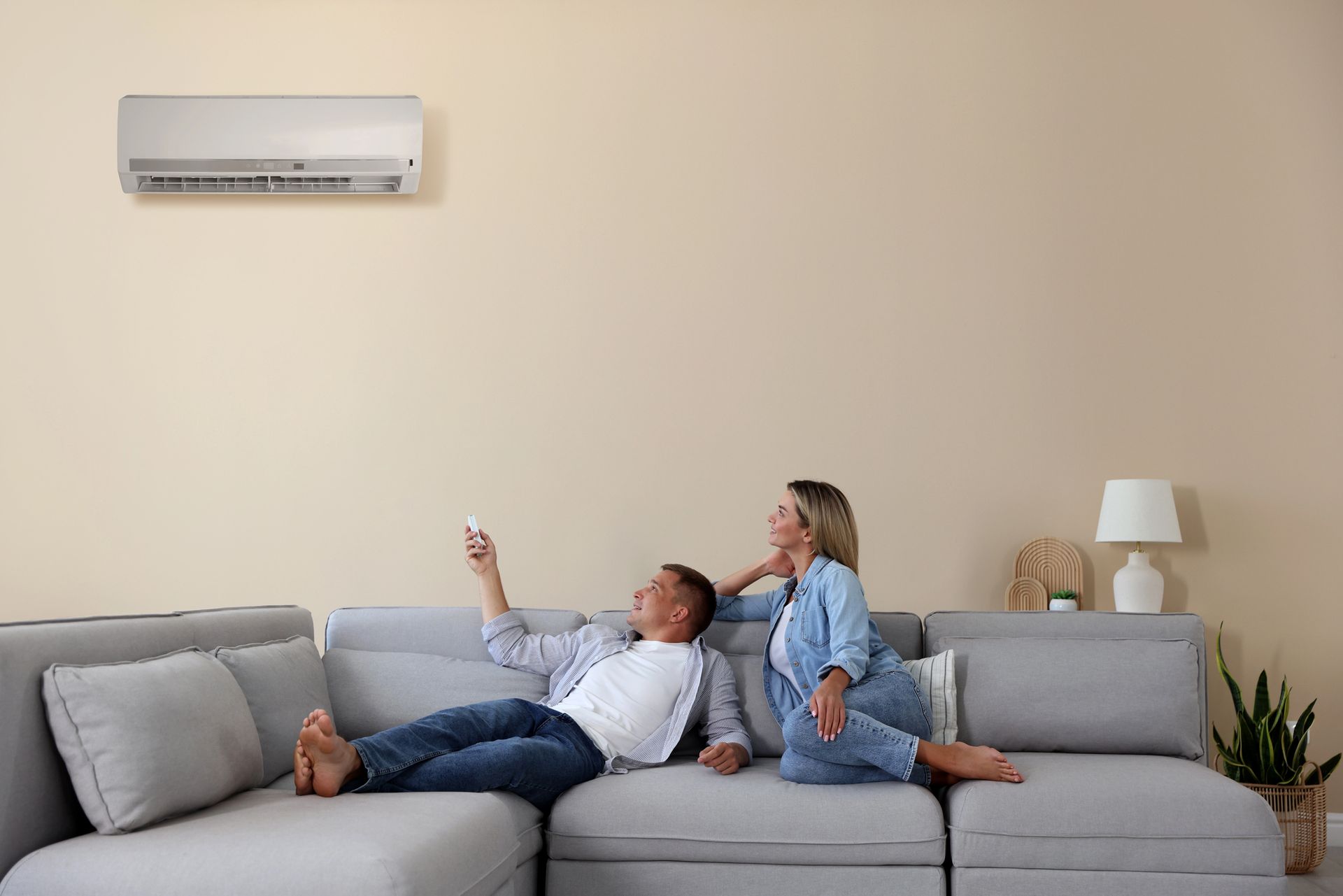 Two people relaxing on a gray sofa in a bright living room, with an air conditioner on the wall.