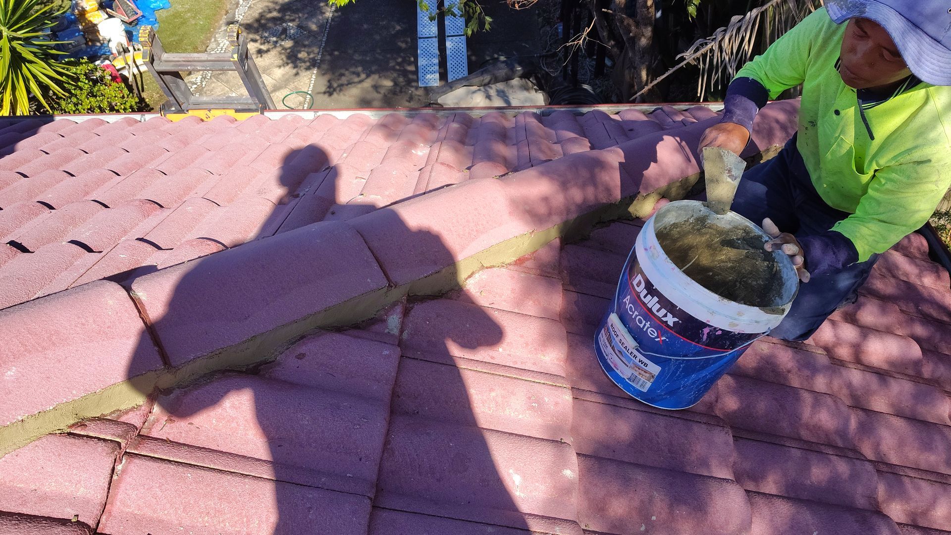 Worker applying roof coating with a bucket on a red shingle roof