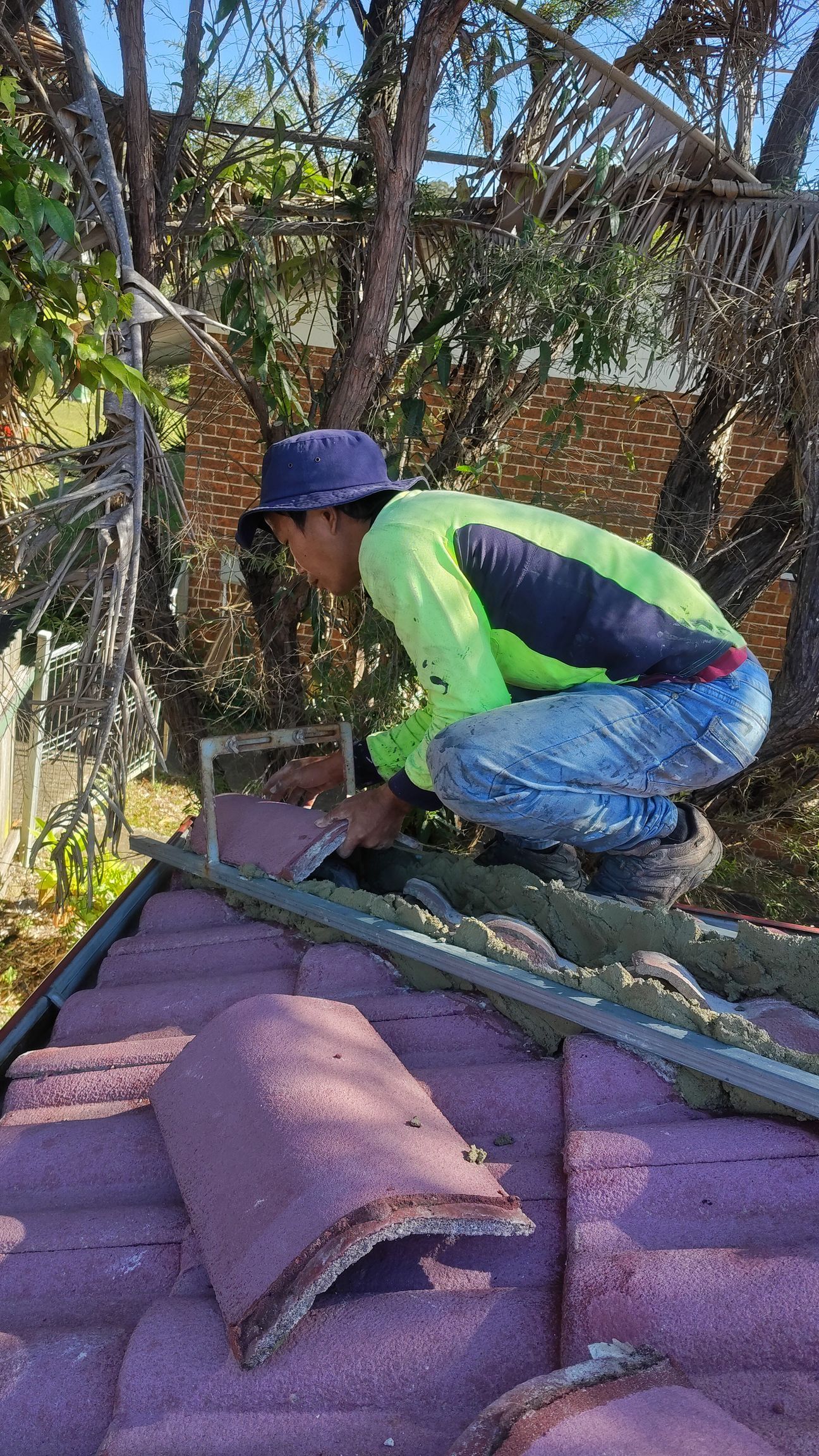 Worker applying roof coating with a bucket on a red shingle roof