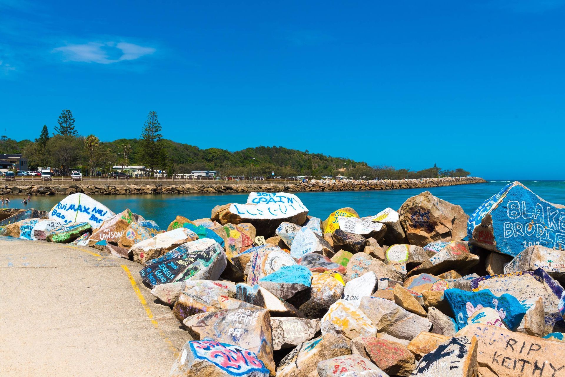 Town Nambucca Head, a colorful graffiti covered rocks line a coastal edge under a bright blue sky.