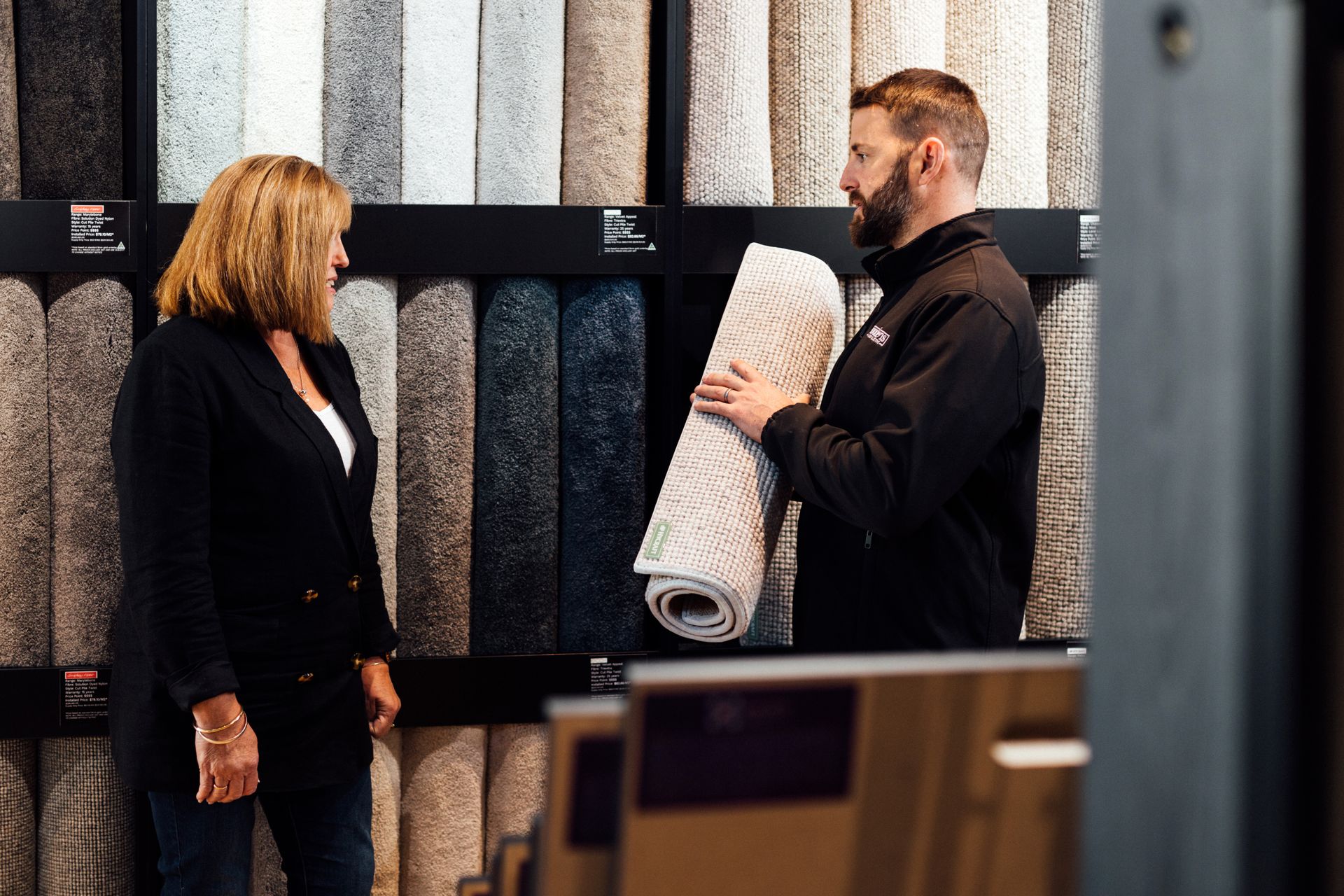 A man is holding a carpet while talking to a woman in a store.