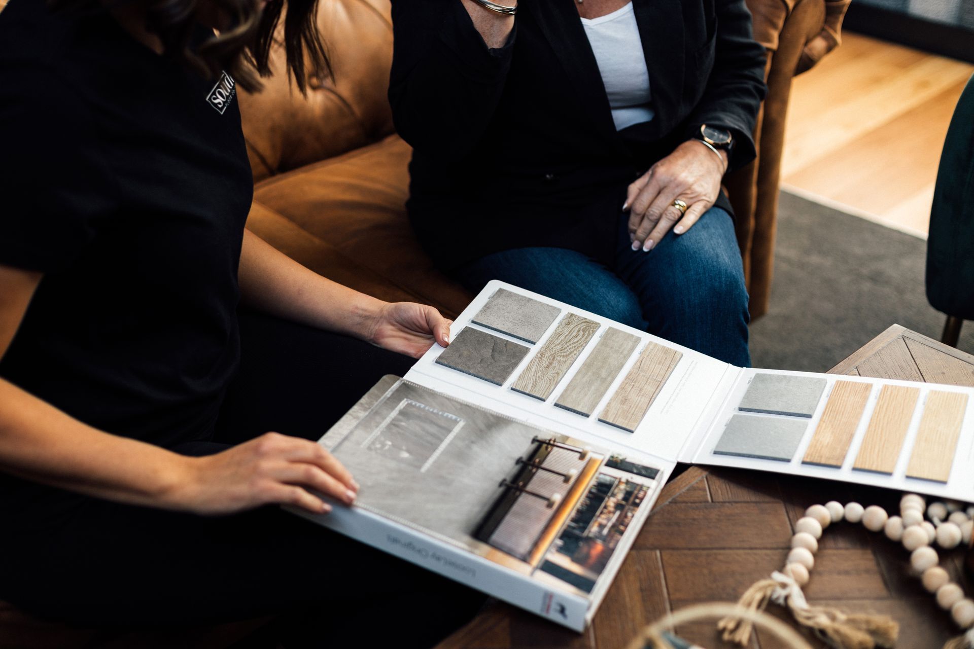 Two women are sitting on a couch looking at a flooring brochure.