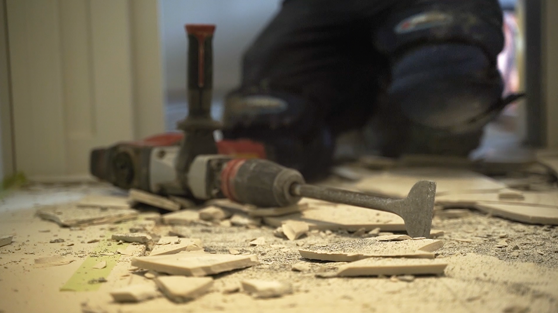 A person is using a hammer to break tiles on the floor.