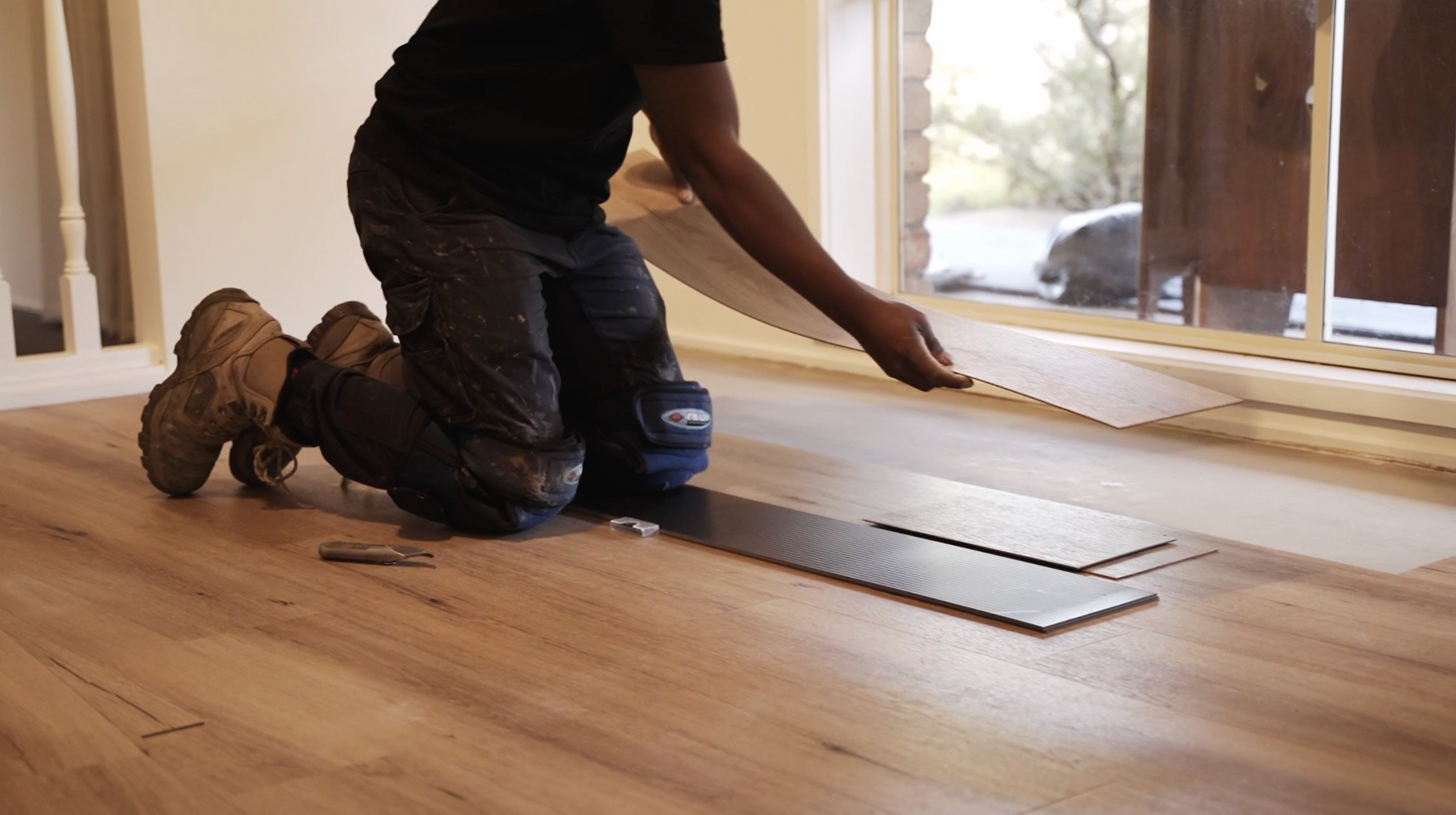 A man is kneeling on the floor while installing a wooden floor.