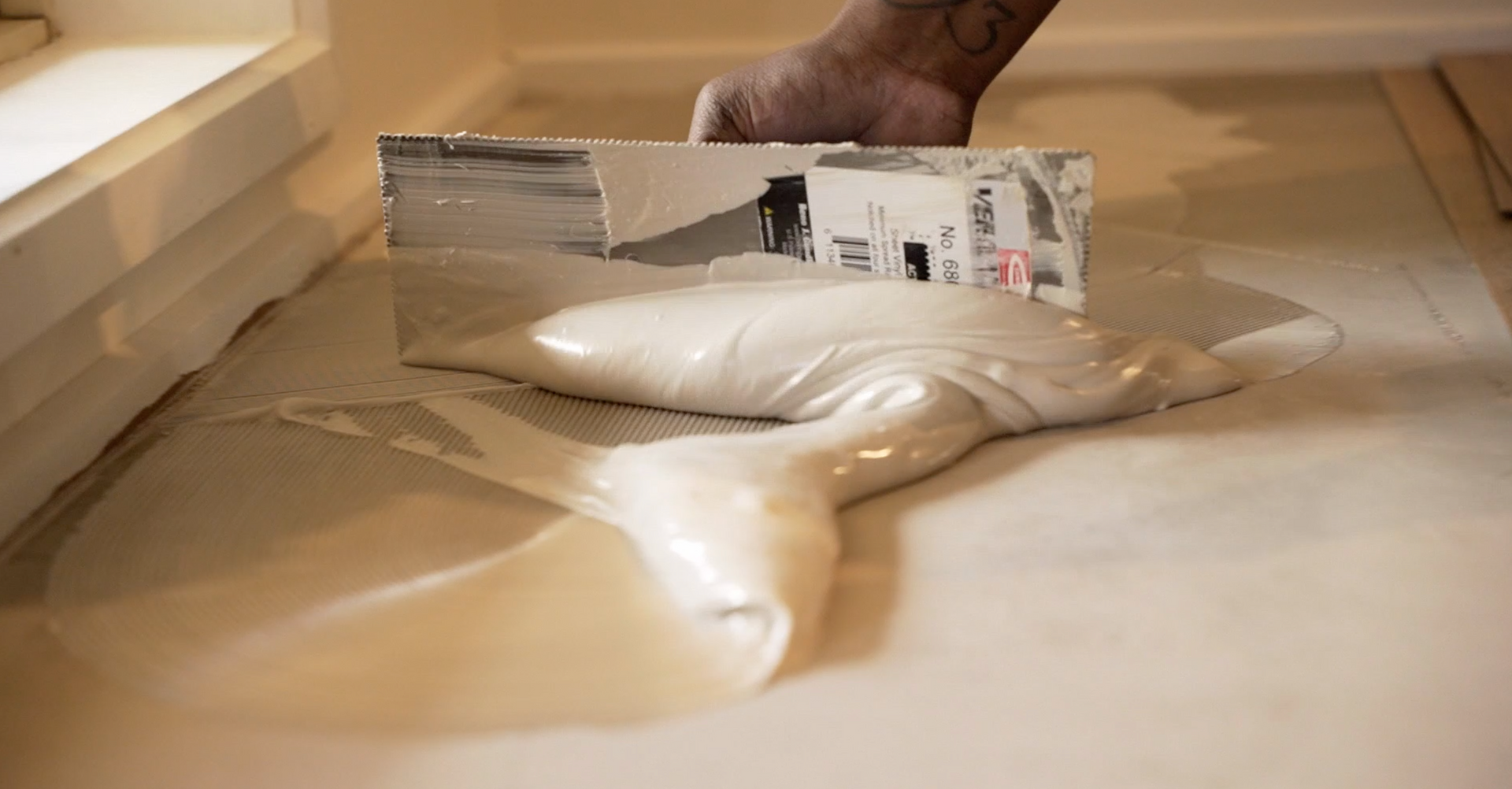 A person is using a spatula to spread a white liquid on the floor.