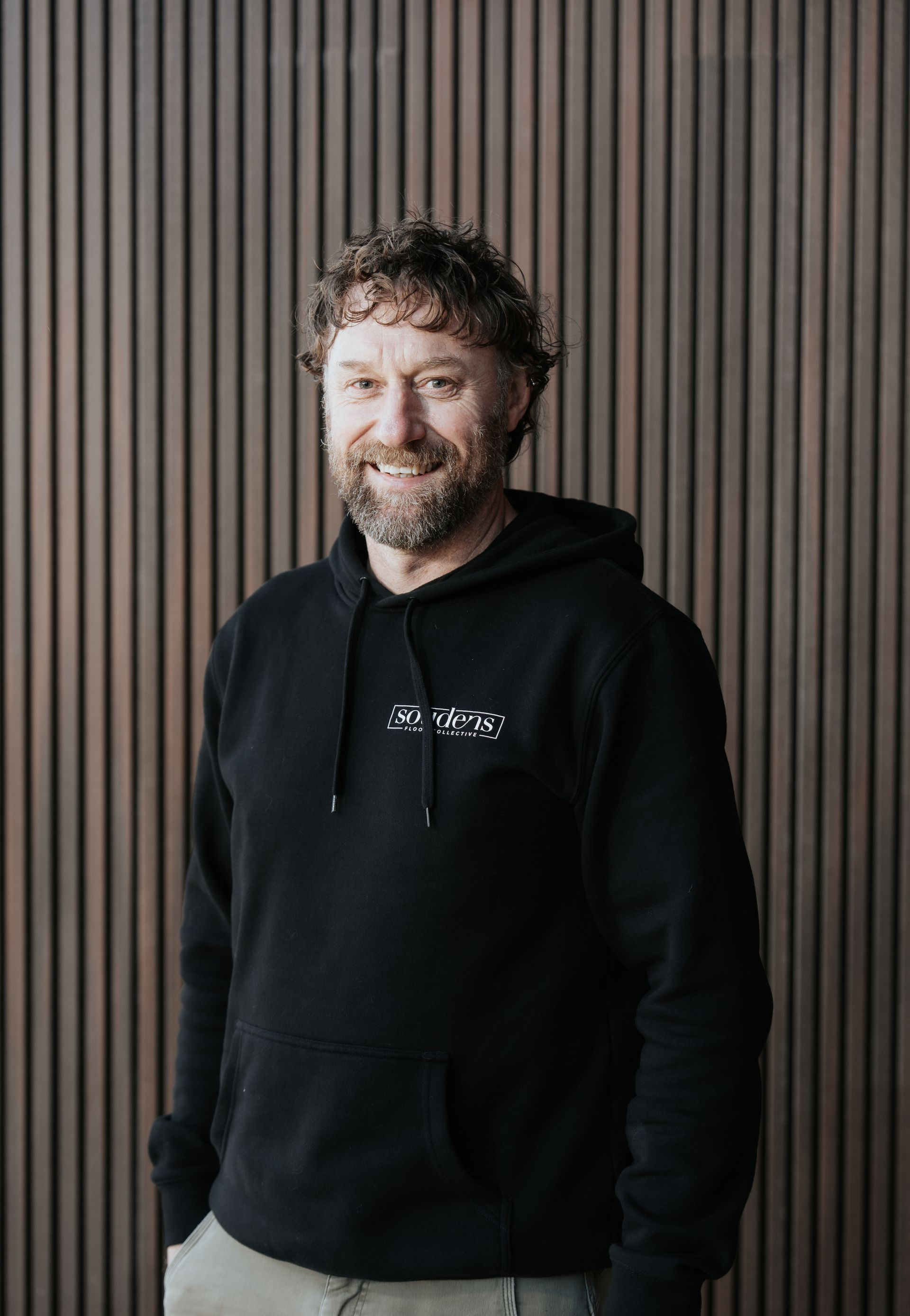 A man with a beard and curly hair is wearing a black jacket.