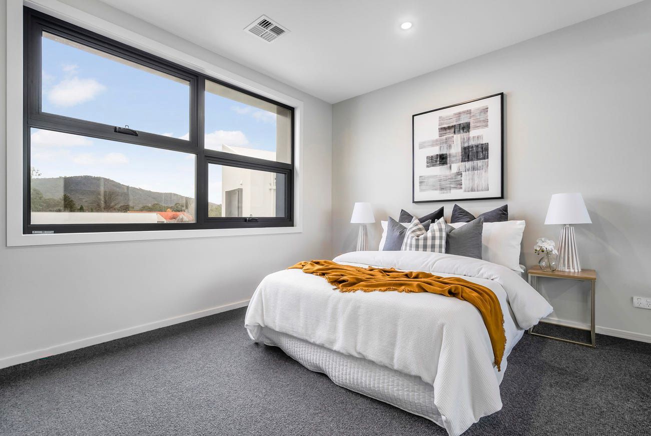A bedroom with a bed , two windows and a painting on the wall.