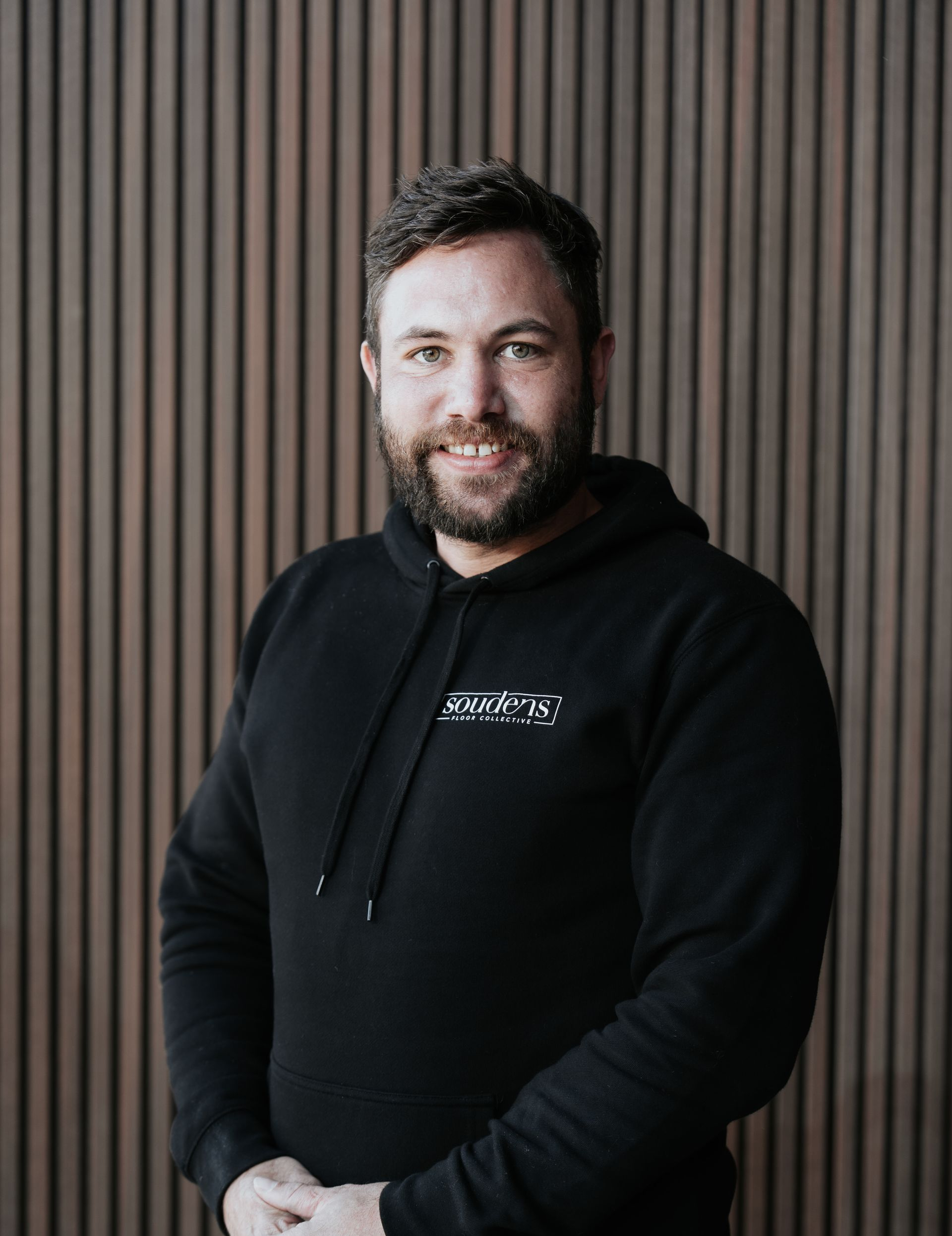 A man with a beard is wearing a black t-shirt and smiling.