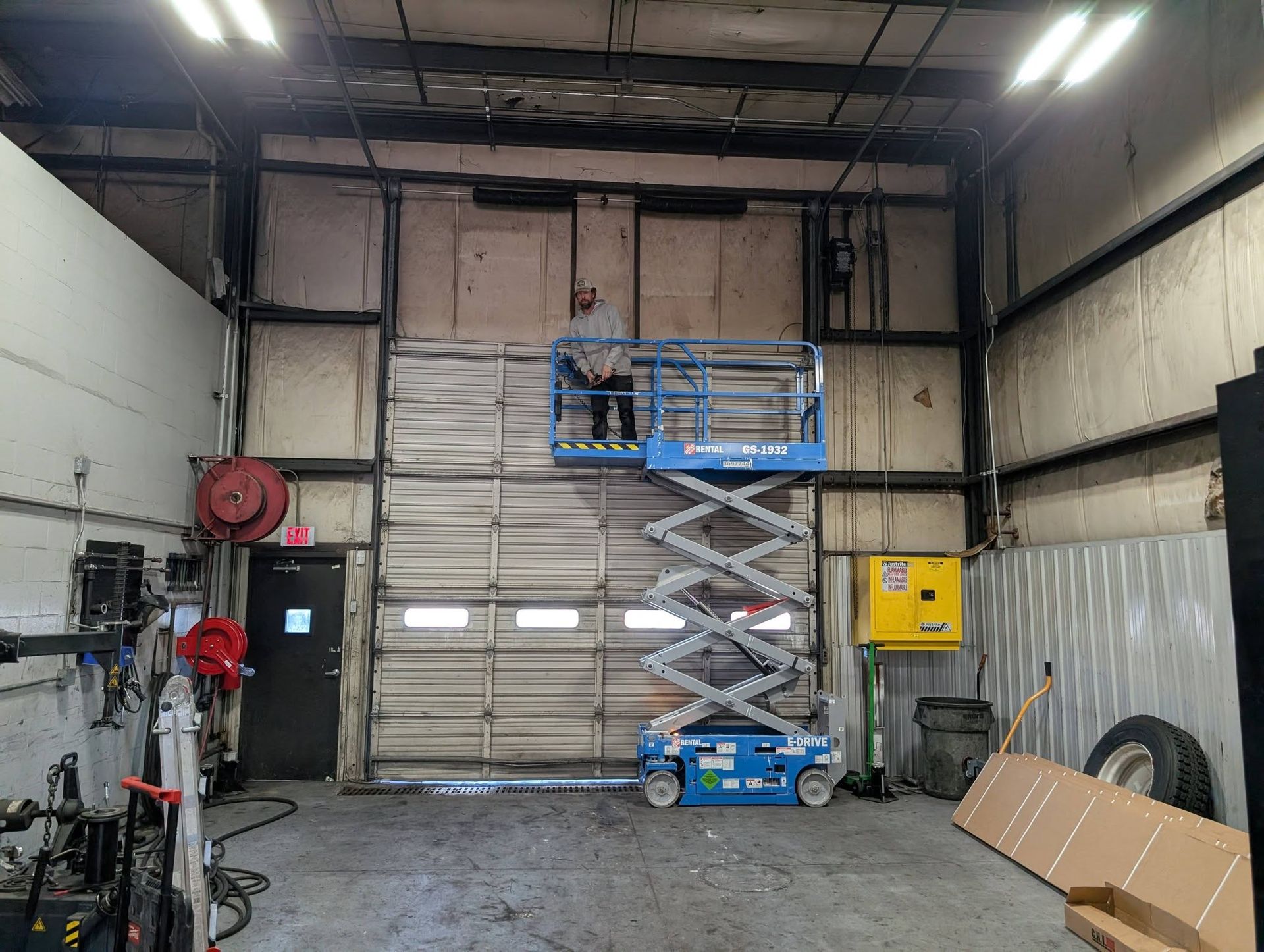 Person on lift working on wall above a closed garage door in a shop.