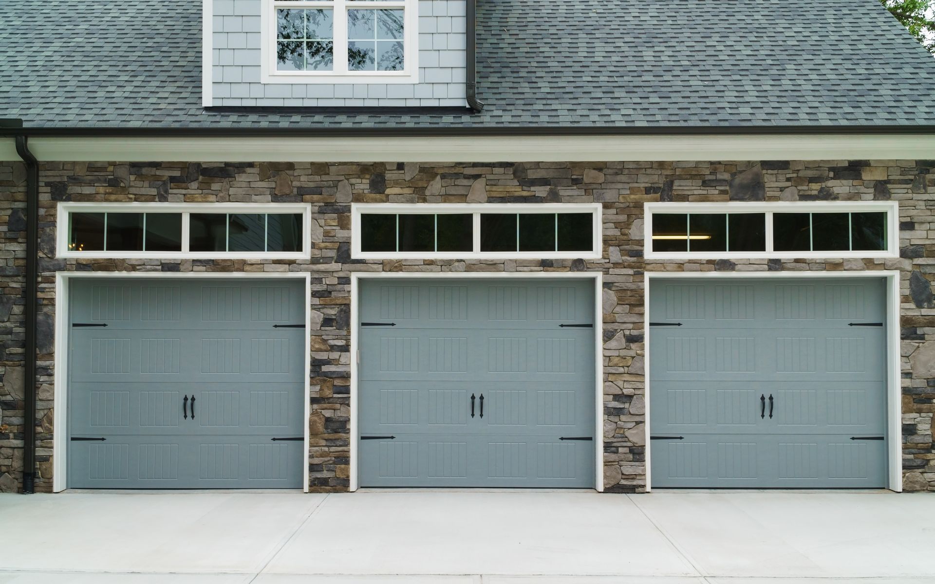 Three gray garage doors with rectangular windows above, set in a stone facade.