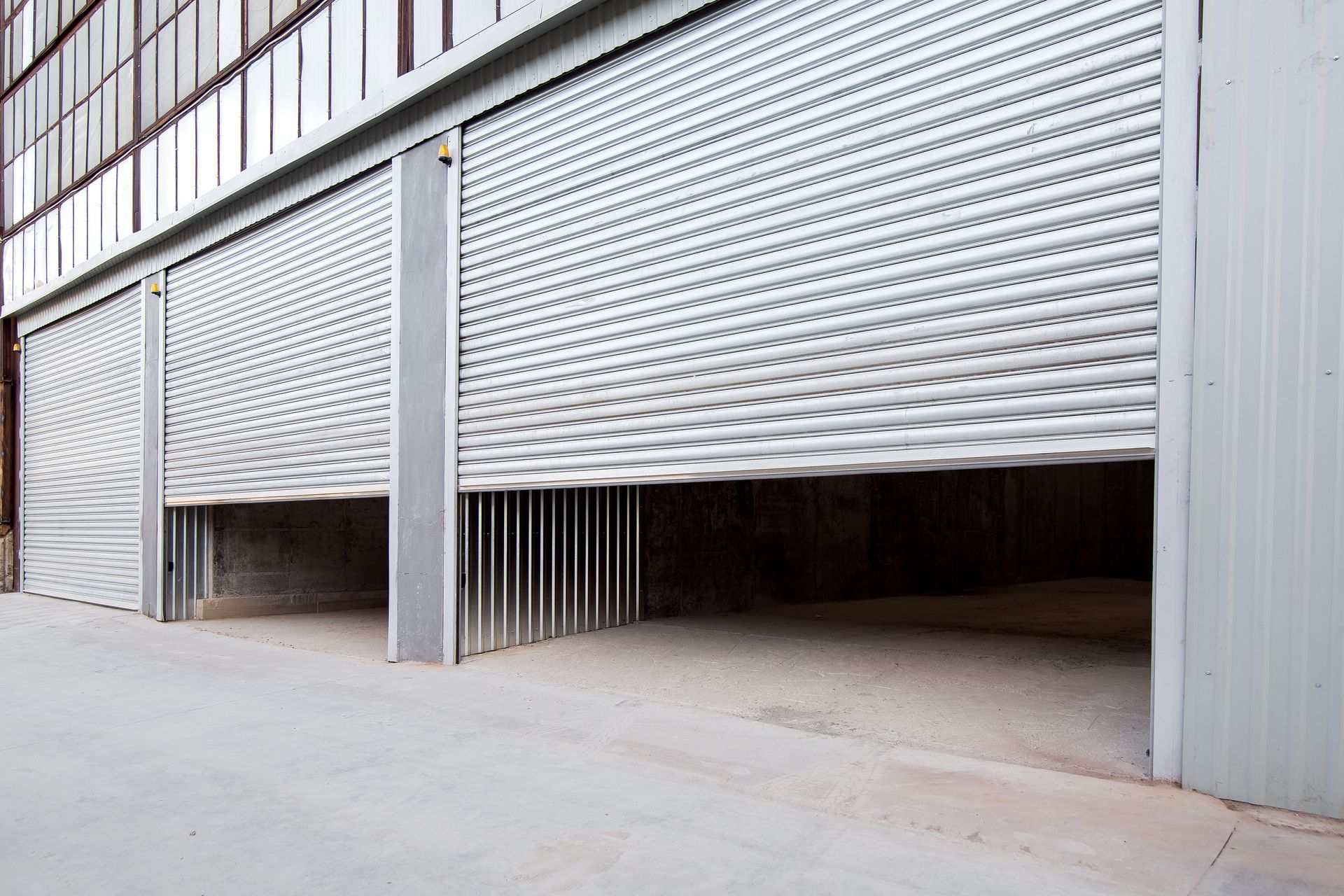 Open warehouse bay doors, silver metal, concrete floor. Open warehouse bay doors, silver metal, concrete floor.