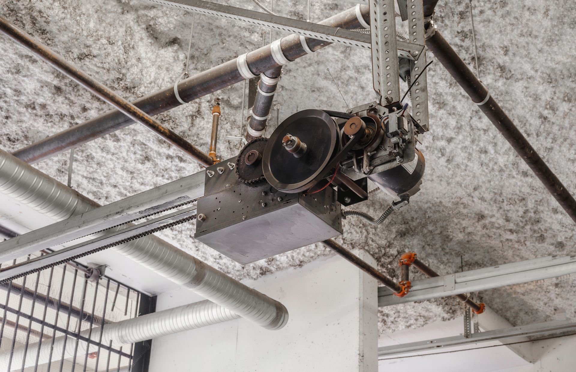 Garage door opener mechanism mounted on a textured ceiling with pipes and ducts. Garage door opener mechanism mounted on a textured ceiling with pipes and ducts.