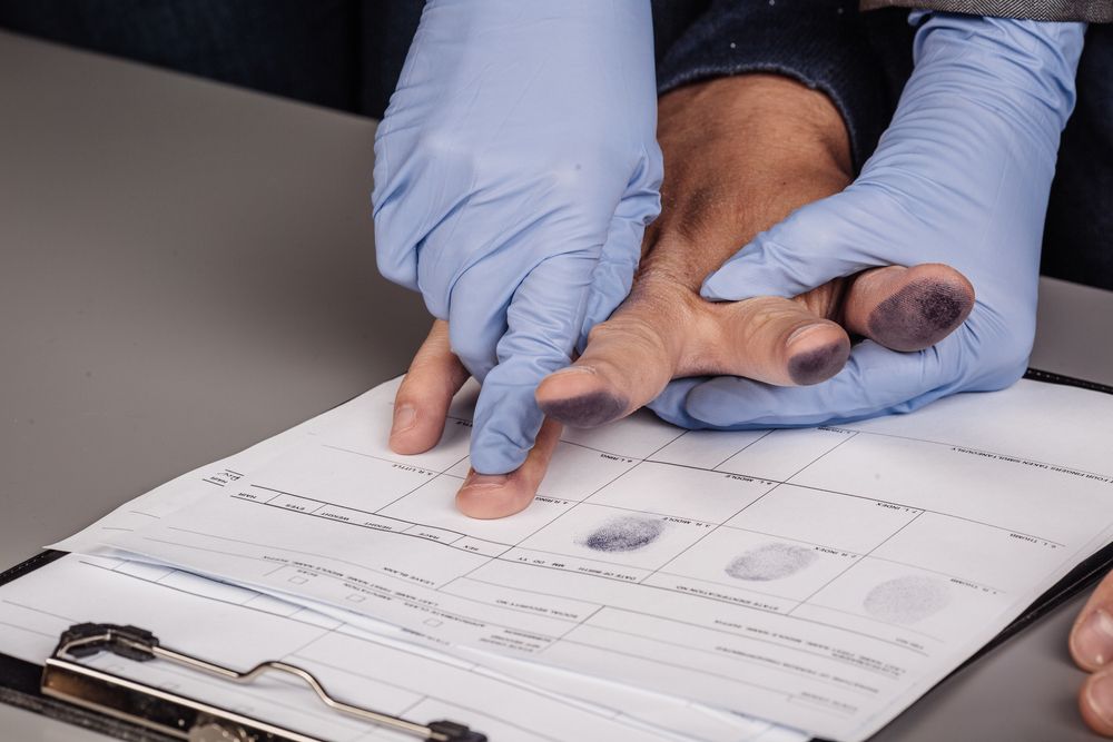 A person wearing blue gloves is taking a fingerprint from a person's hand