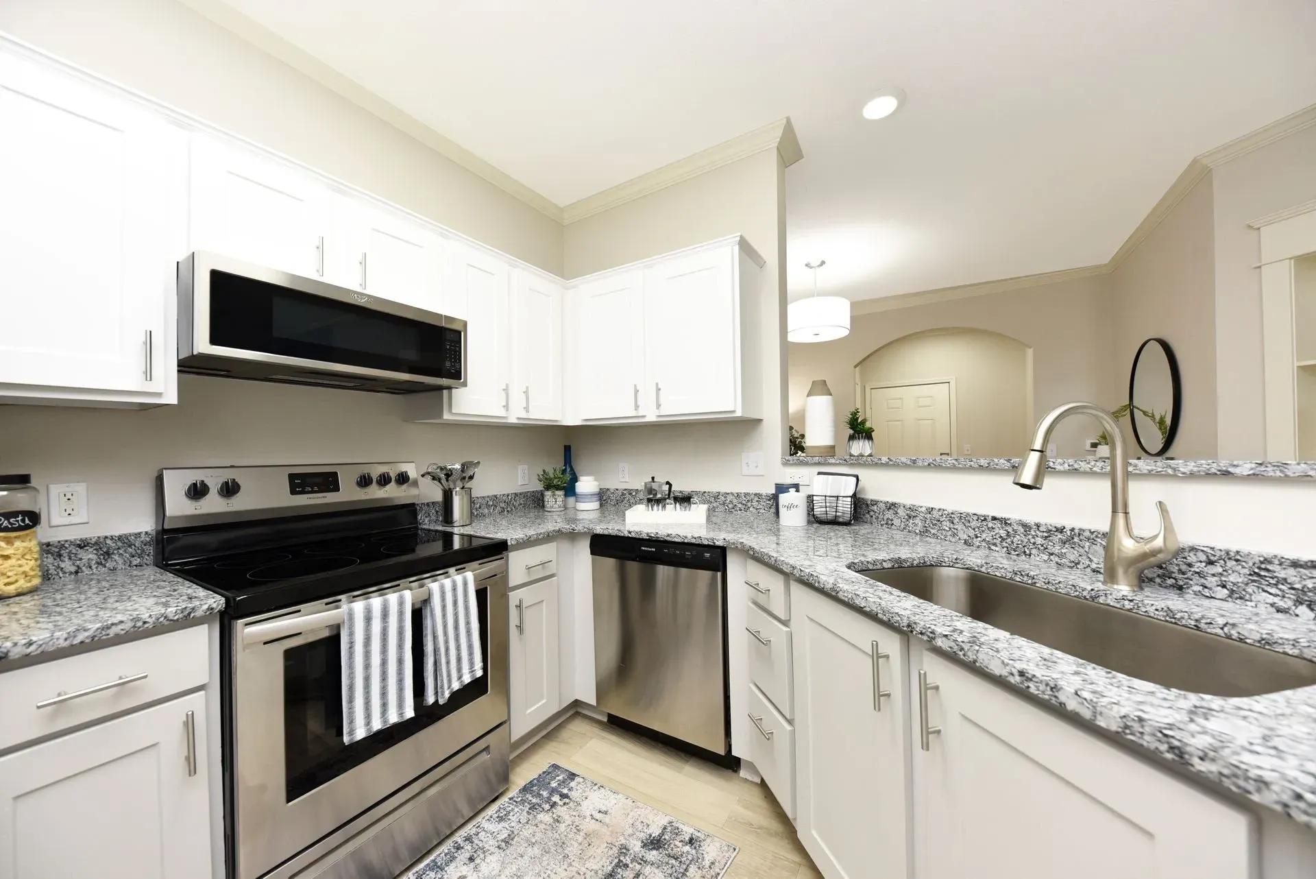 Modern kitchen with white cabinets, granite countertops, stainless steel appliances, and a large sink.