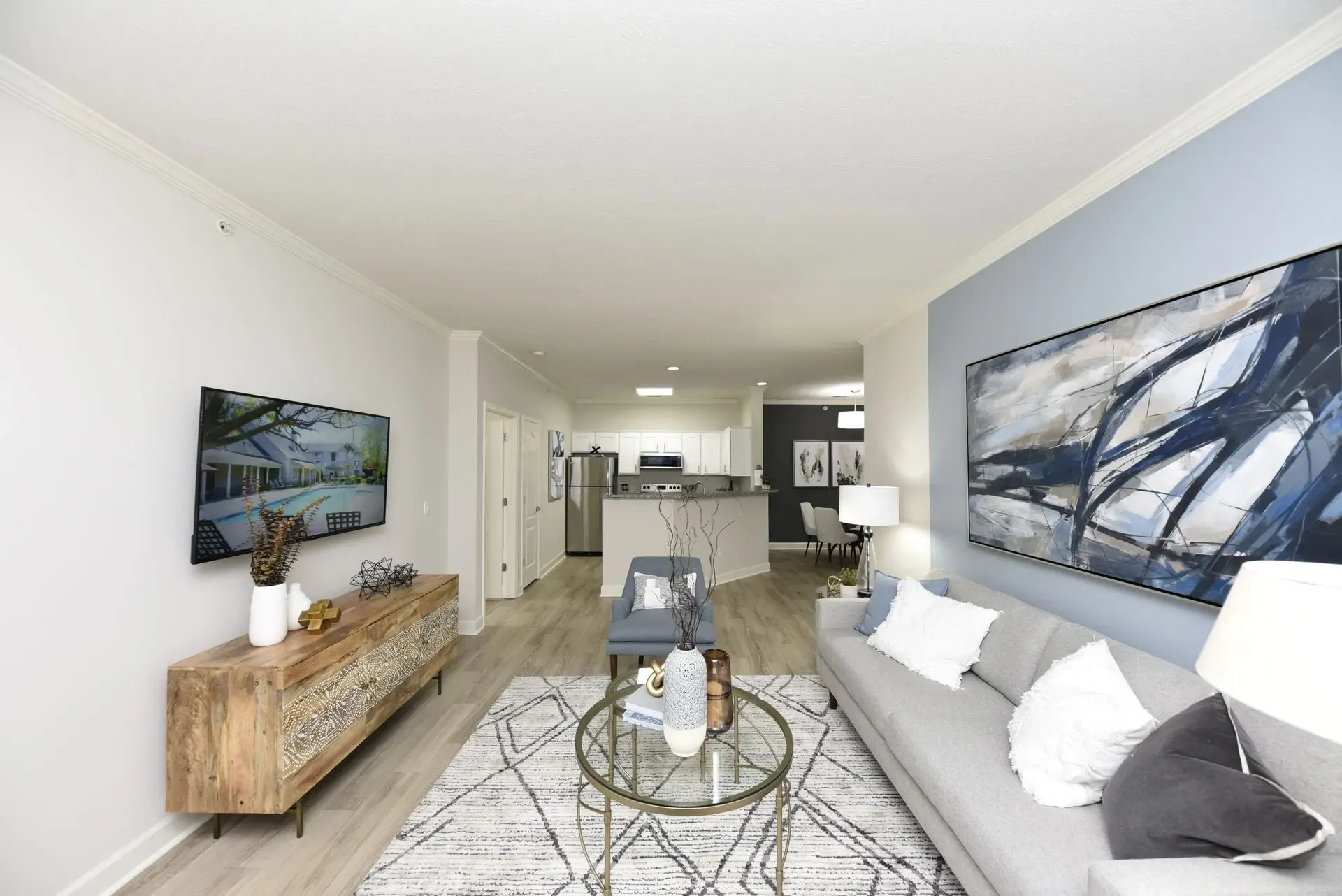 Modern living room with gray couch, coffee table, TV, and open kitchen view.