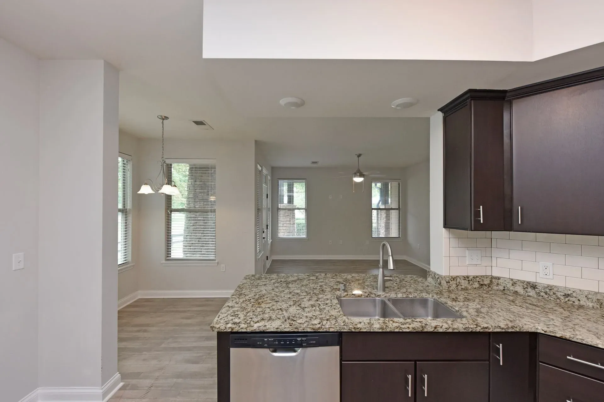 Modern kitchen with granite countertops, stainless steel sink and dishwasher, dark wood cabinets, and subway tile backsplash.