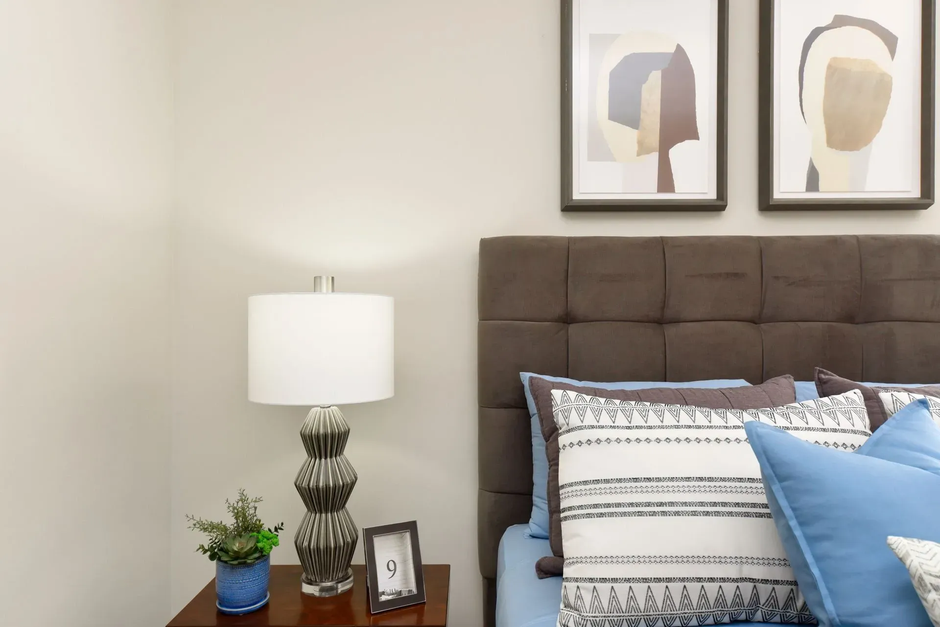 Close-up of a bedroom with a modern lamp and decorative pillows on a bed.