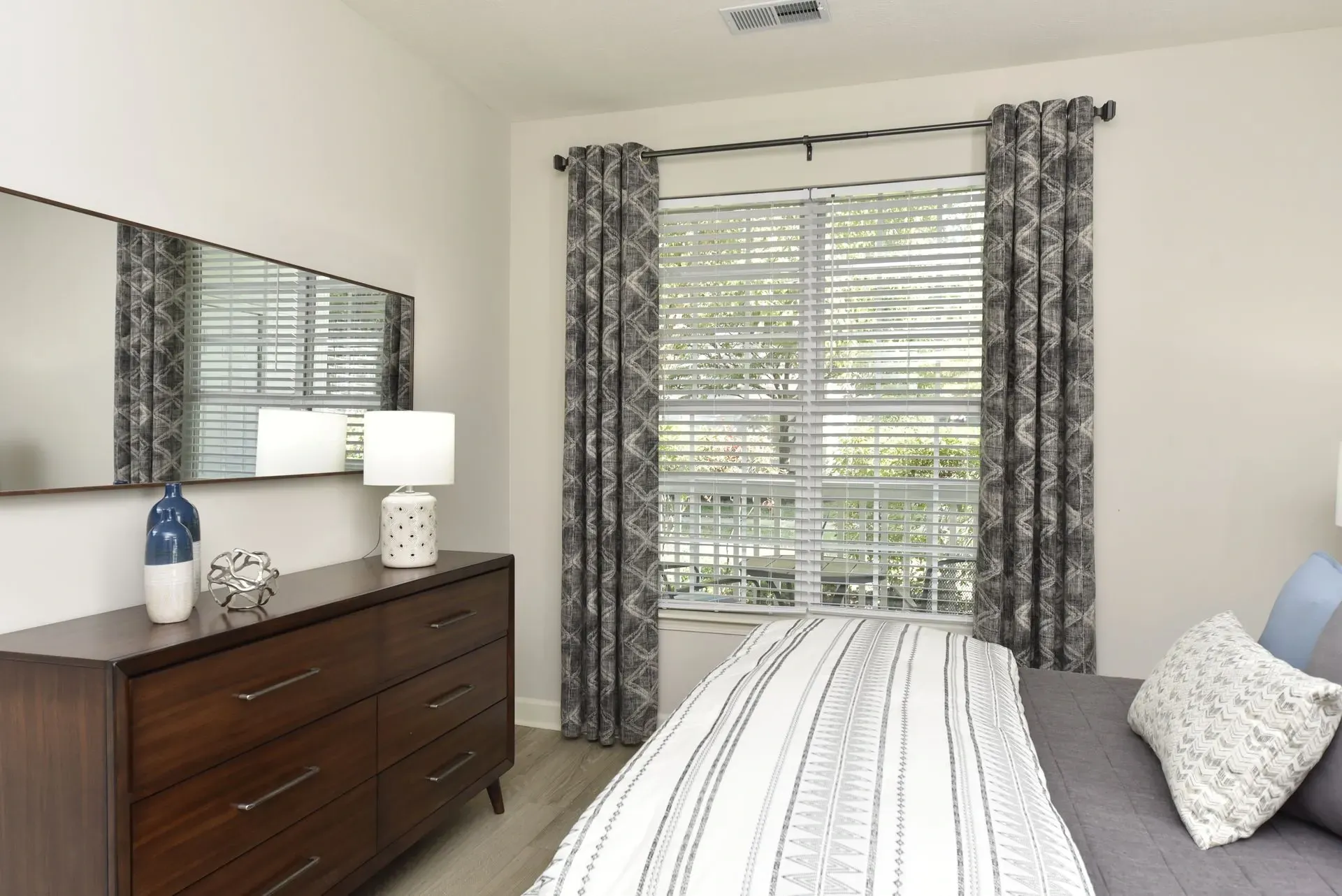 Bedroom with a dresser, mirror, and window with blinds.