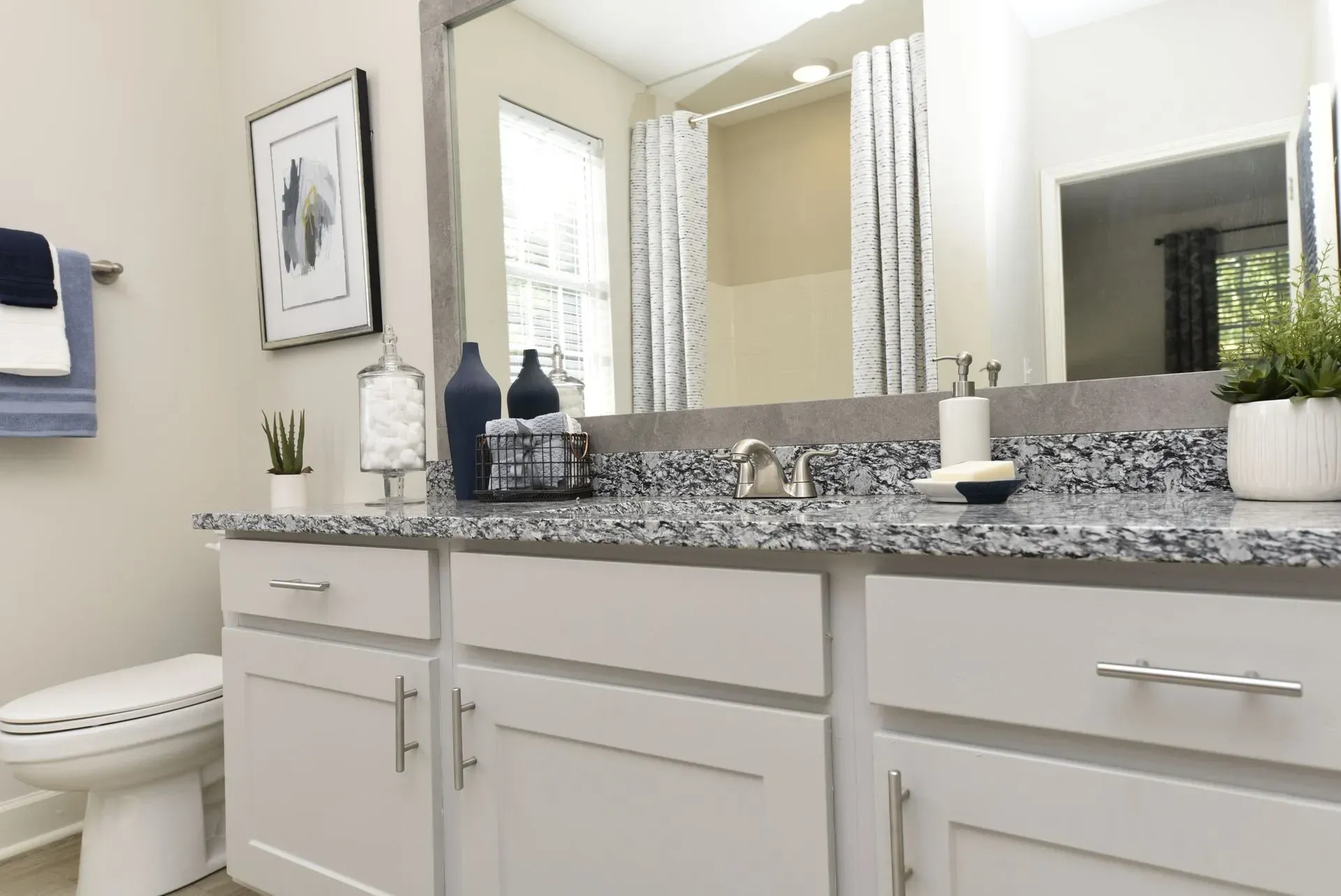 Modern bathroom vanity with granite countertop, white cabinets, and toilet.