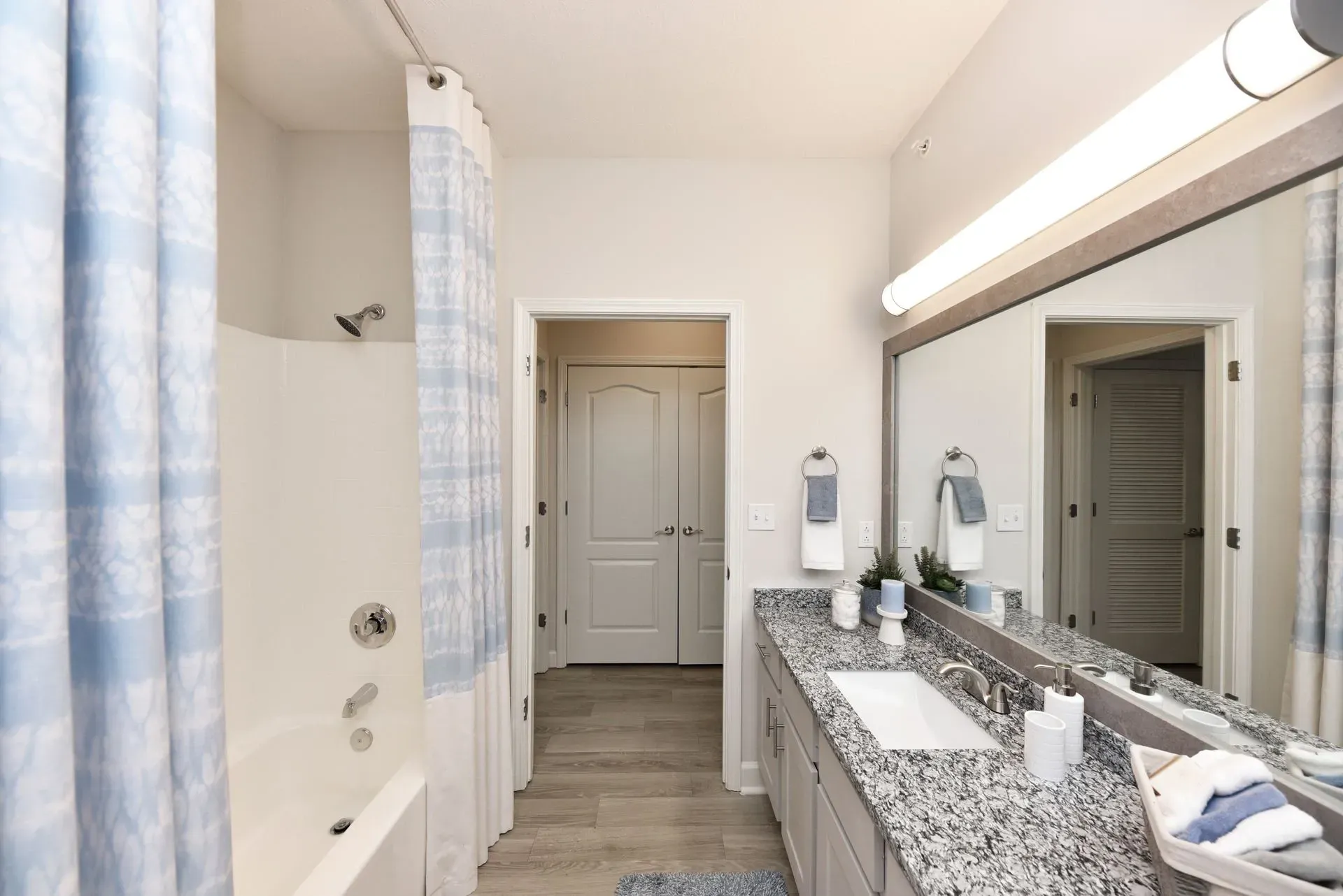 Modern bathroom with a white bathtub, shower with blue patterned curtain, granite countertop, and vanity with large mirror.
