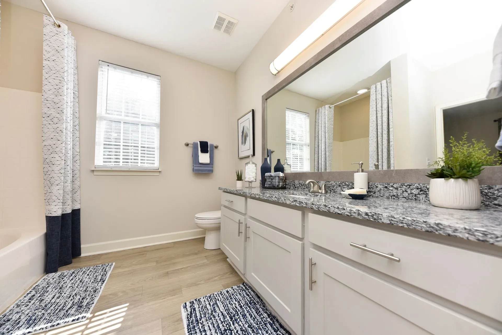 Bathroom vanity with granite countertop and double sinks, toilet, and bathtub with shower curtain.