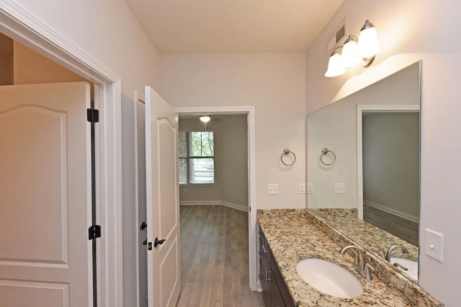 Bathroom vanity with granite countertop and a large mirror. Doorway leads to a bedroom.