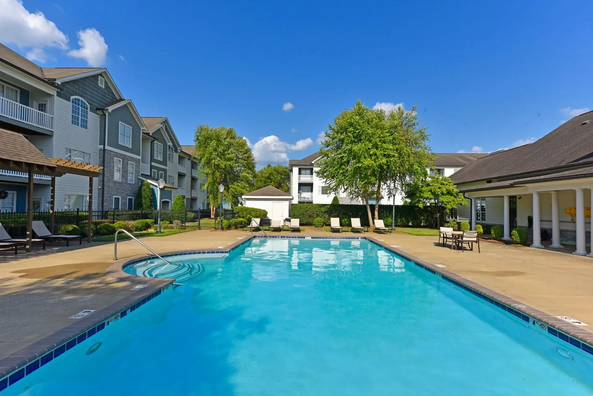 Outdoor swimming pool with lounge chairs and apartment buildings in the background.