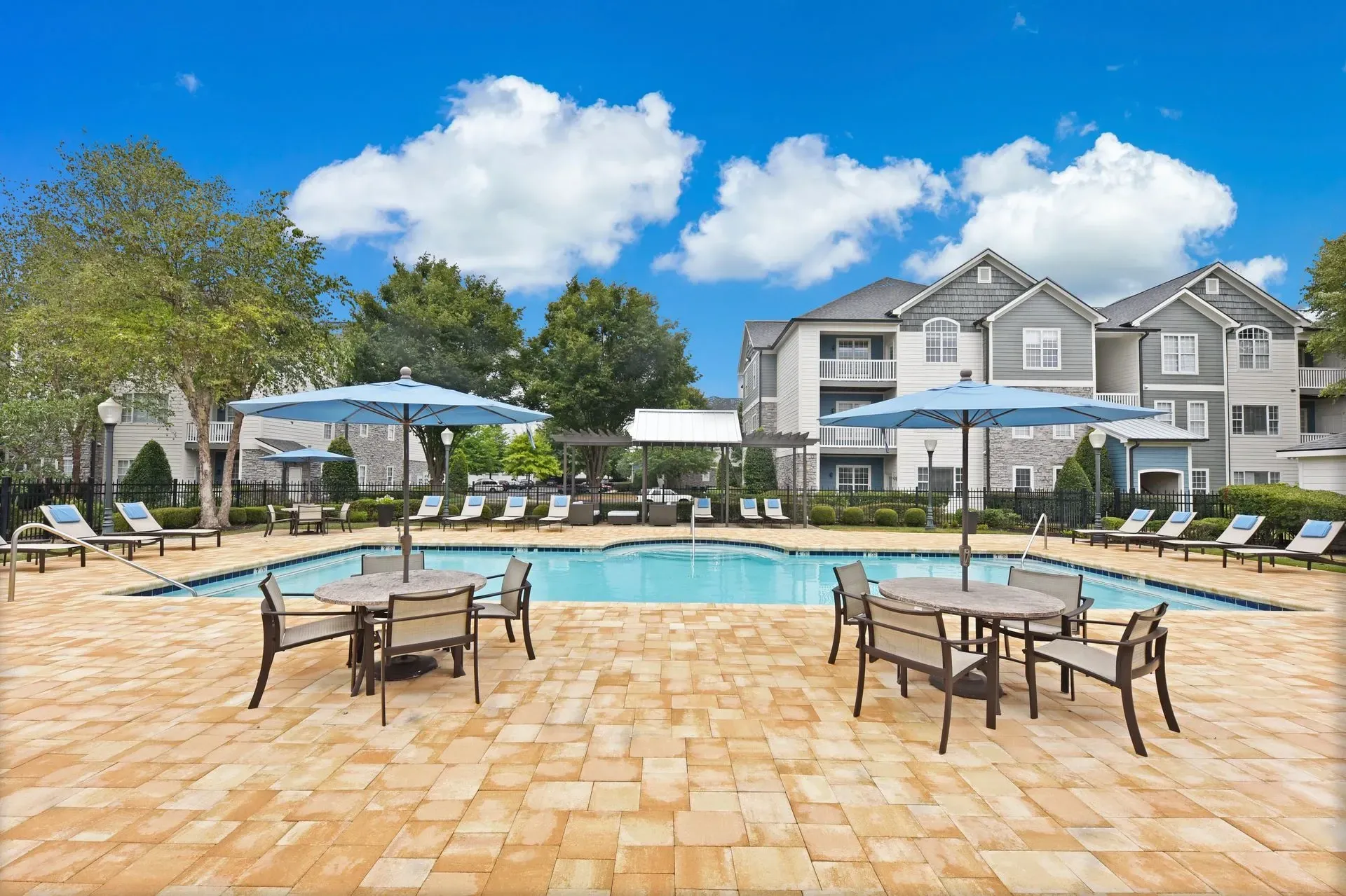 Apartment complex swimming pool area with lounge chairs and tables under umbrellas.