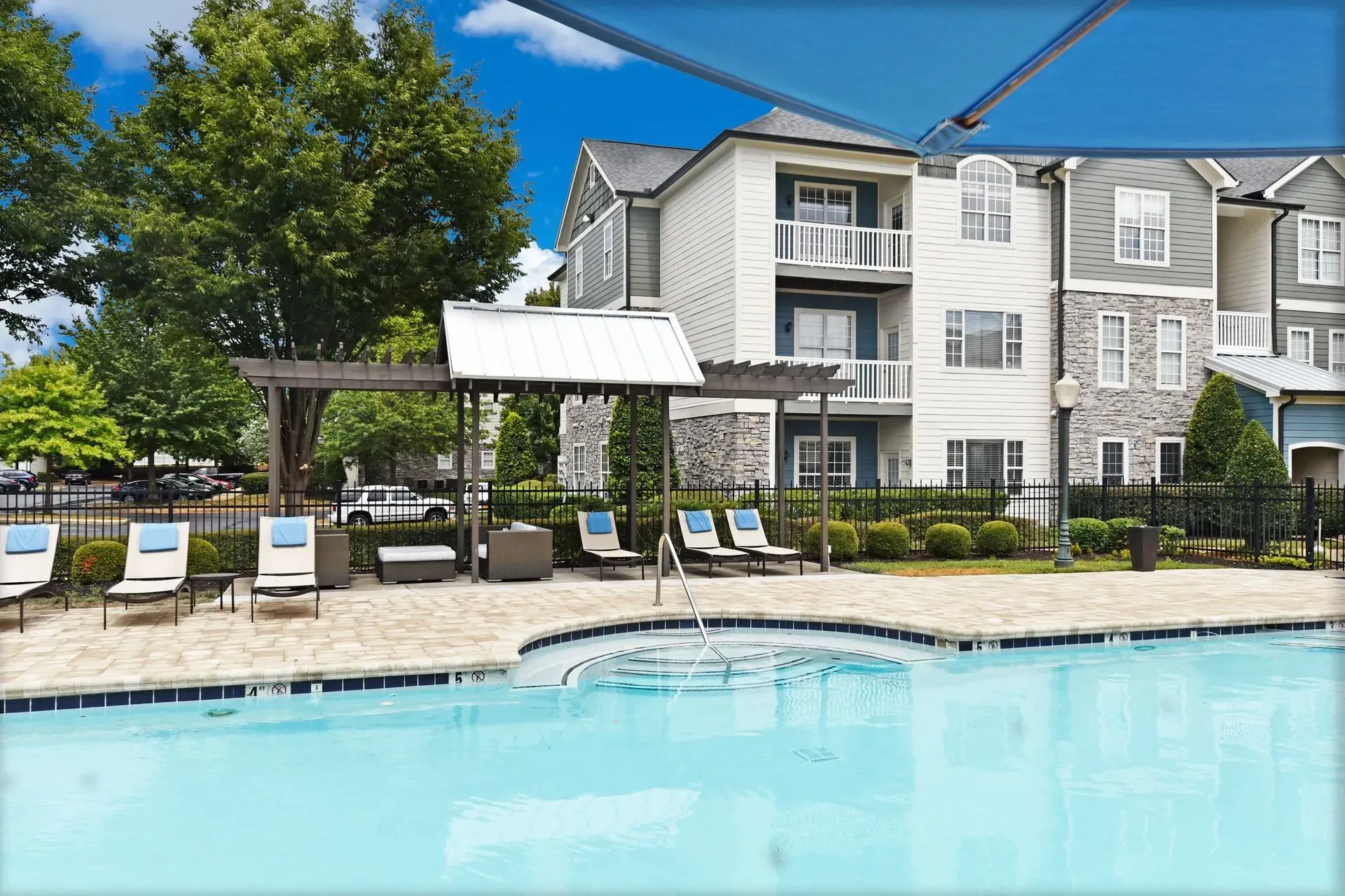 Outdoor swimming pool and jacuzzi with lounge chairs and apartment buildings in the background.