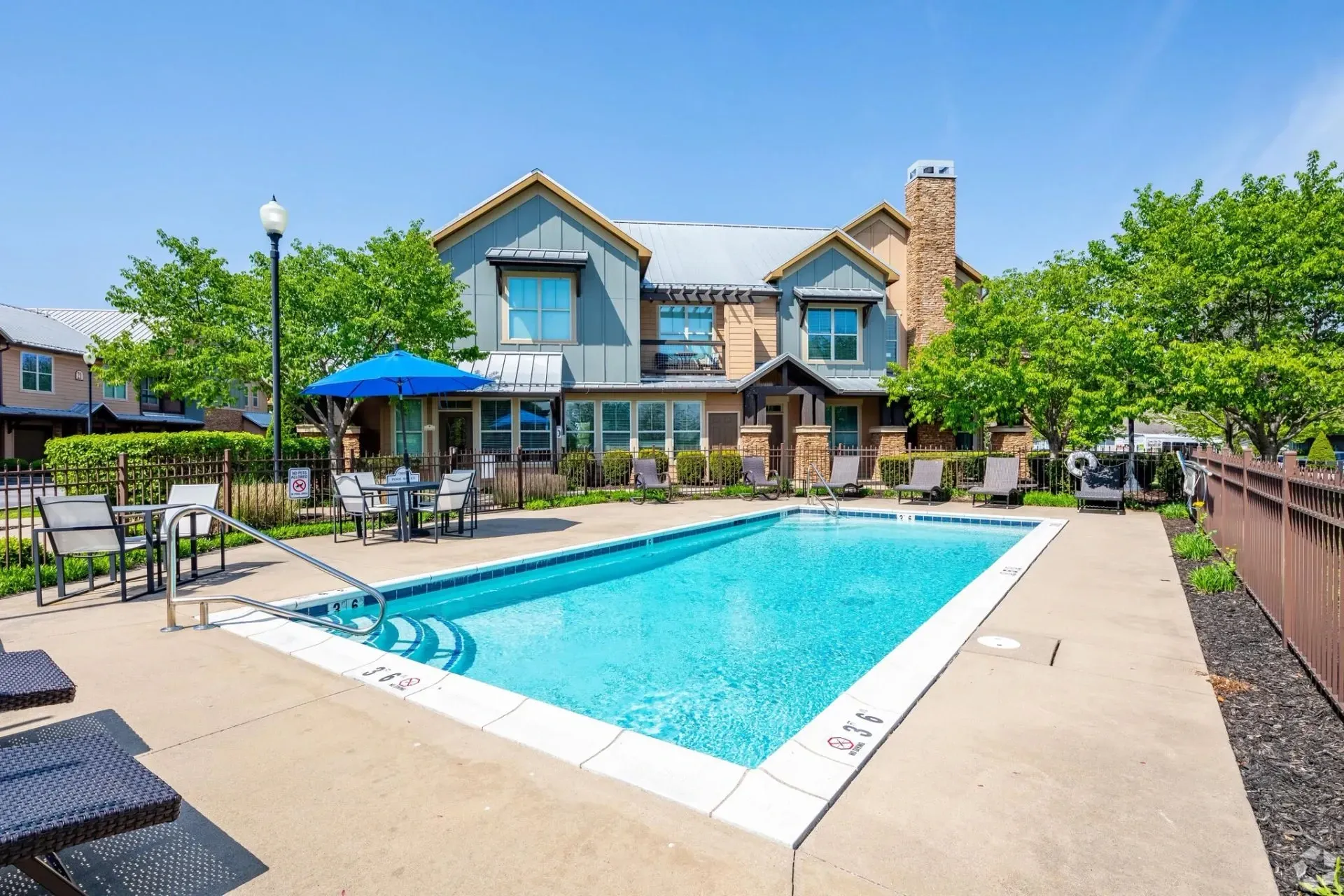 Outdoor swimming pool with lounge chairs and seating areas, with apartment buildings in the background.