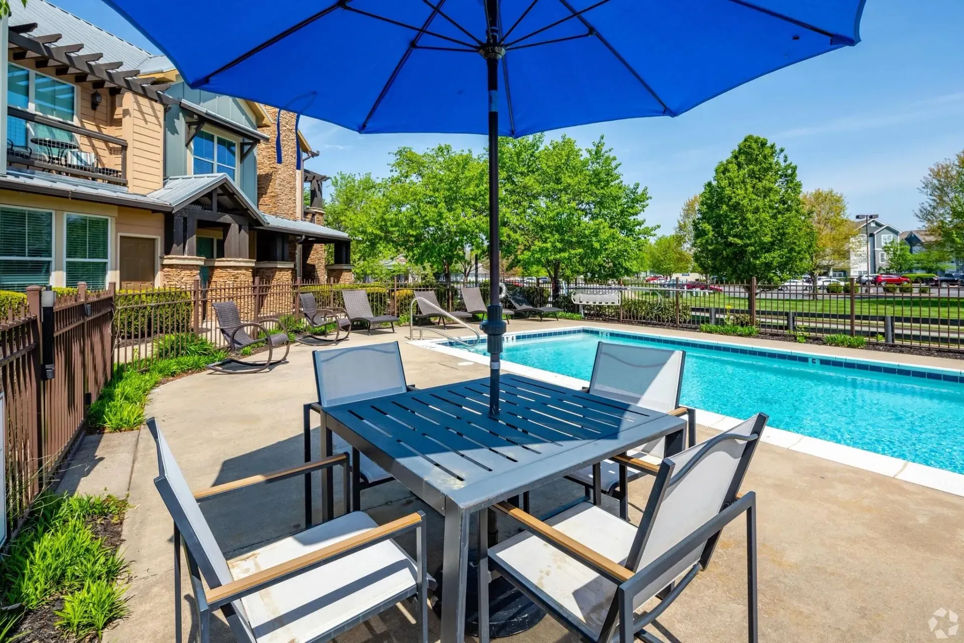 Outdoor swimming pool with lounge chairs and a table with chairs under a blue umbrella.