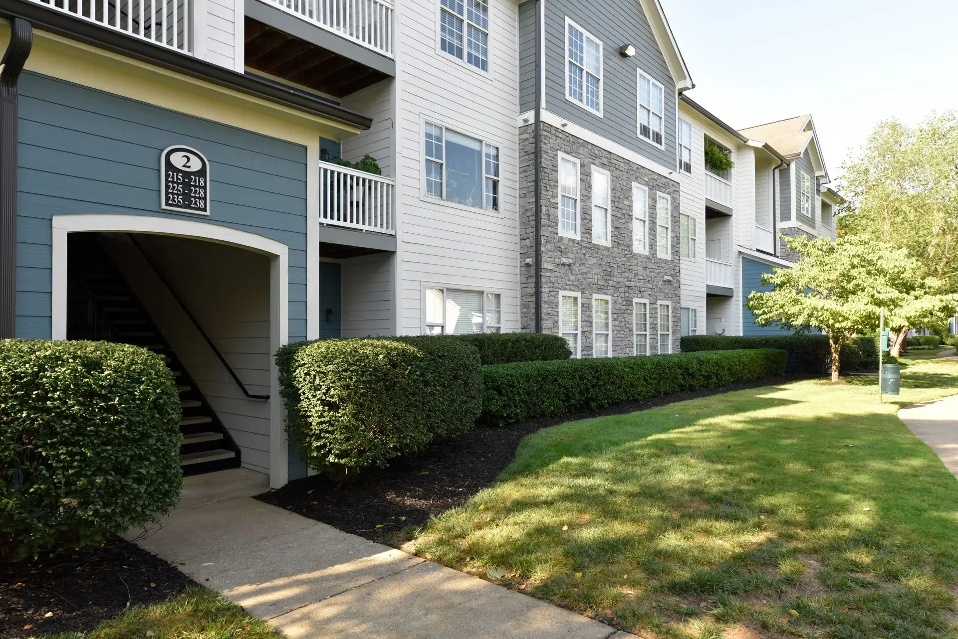 Exterior view of apartment building with covered staircase and manicured hedges.