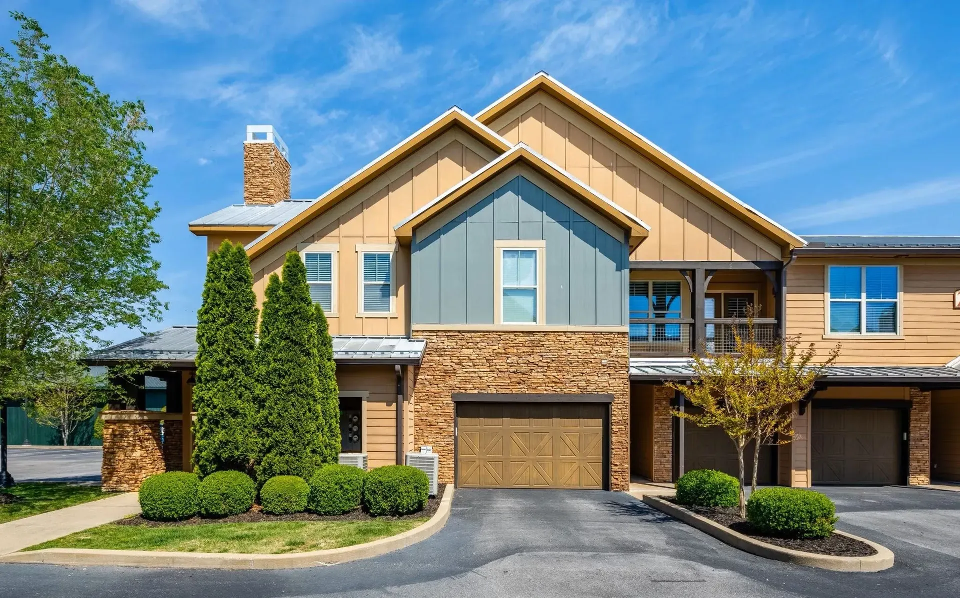 Exterior view of a multifamily property with attached garages, stone accents, and manicured landscaping.