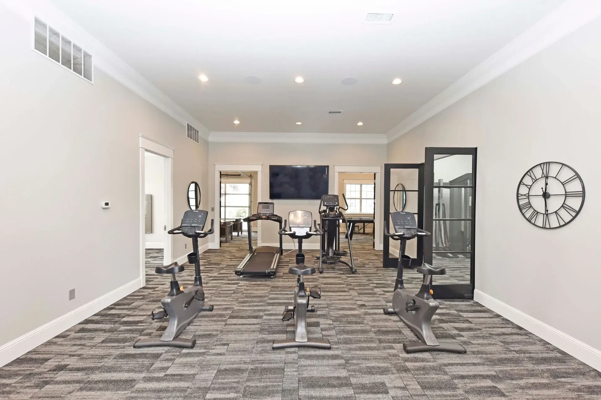Gym with treadmills and stationary bikes, flat screen TV, and large clock