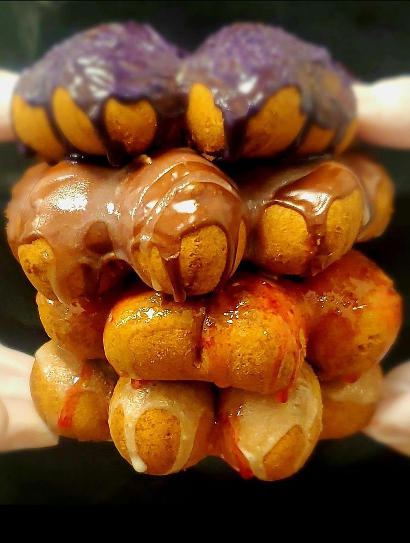Stack of glossy purple and orange pastries with segmented shells, held in a hand