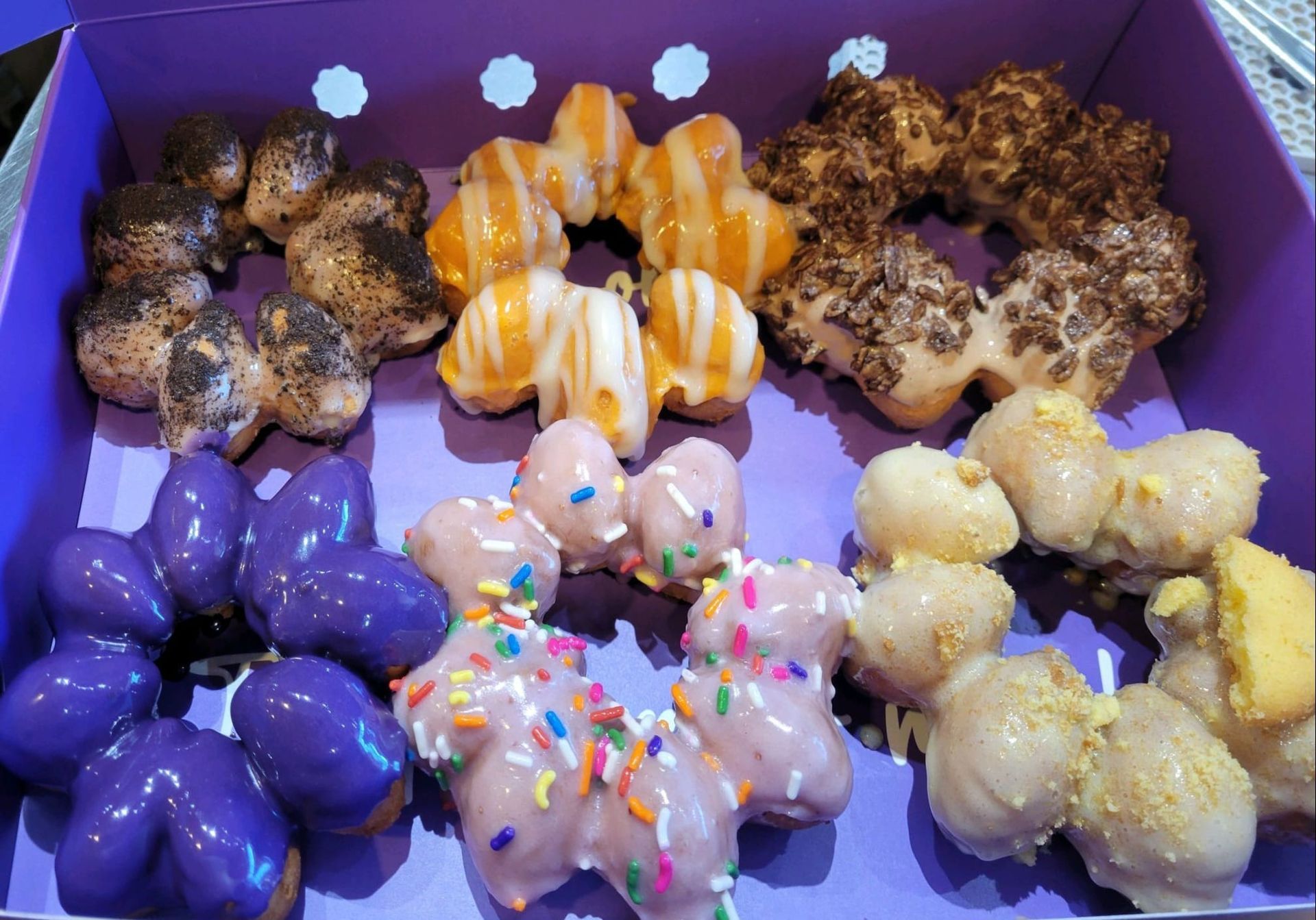 Assorted colorful iced pastries and donuts arranged in a purple box