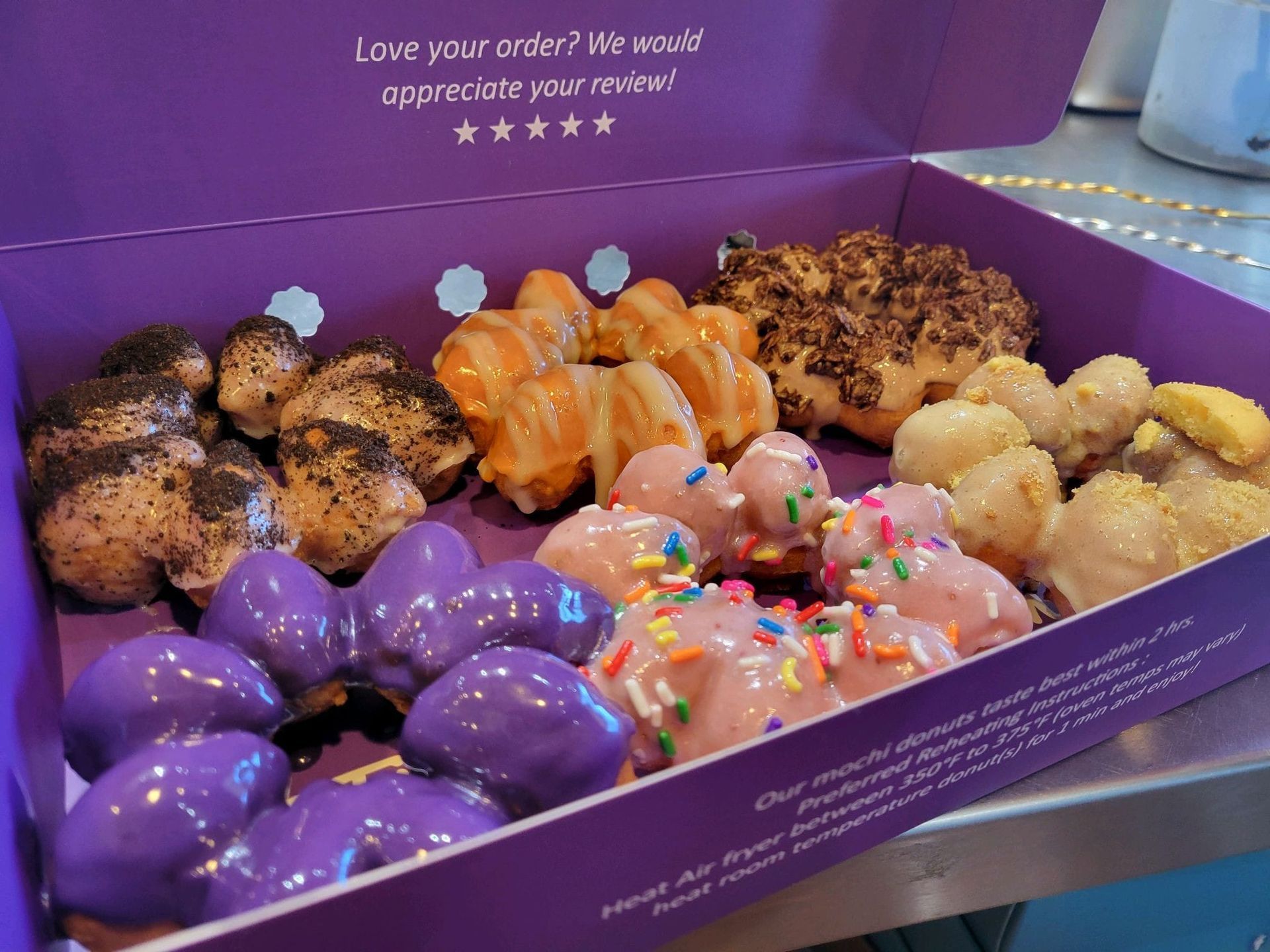 Assorted colorful pastries in a purple box, including glazed, frosted, and powdered donuts.