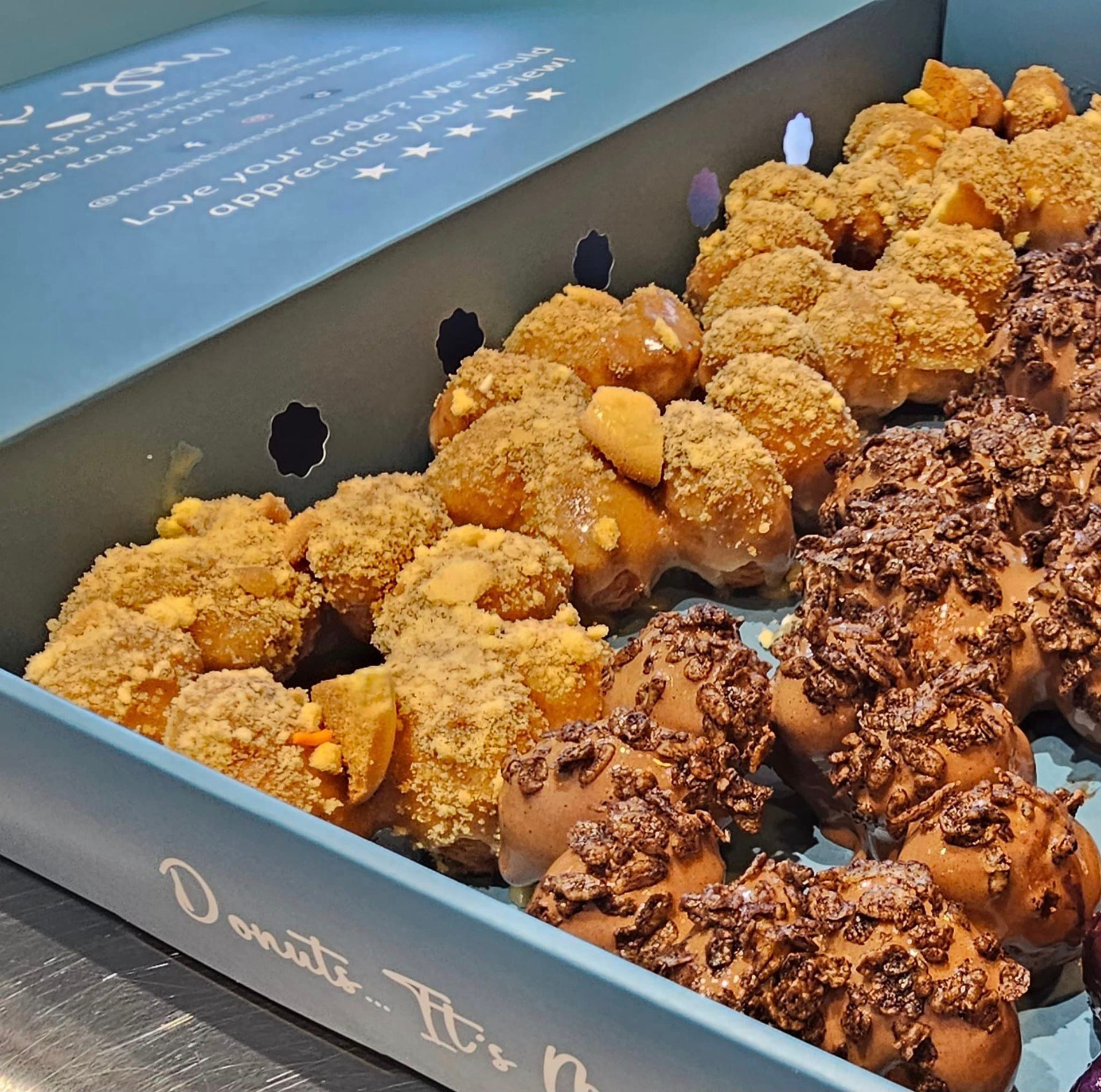 Assorted glazed and sprinkled donuts in a blue pastry box